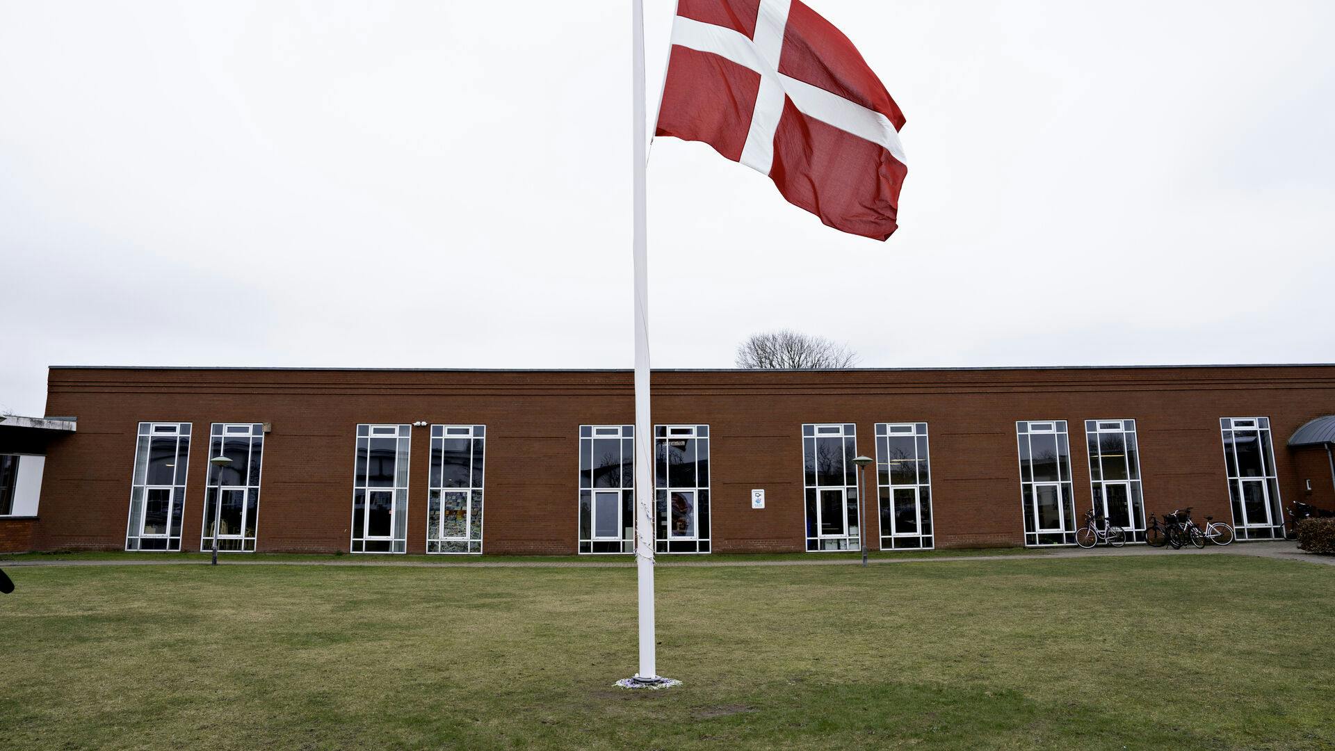 Der flages på halv stang ved Hjallerup Skole i Nordjylland tirsdag den 12. marts 2024. En 17-årig dreng er anholdt i sag om drab på 13-årig pige i Hjallerup, oplyser politiet. Ved foden af flagstamgen ligger blomster. (Foto: Henning Bagger/Ritzau Scanpix)