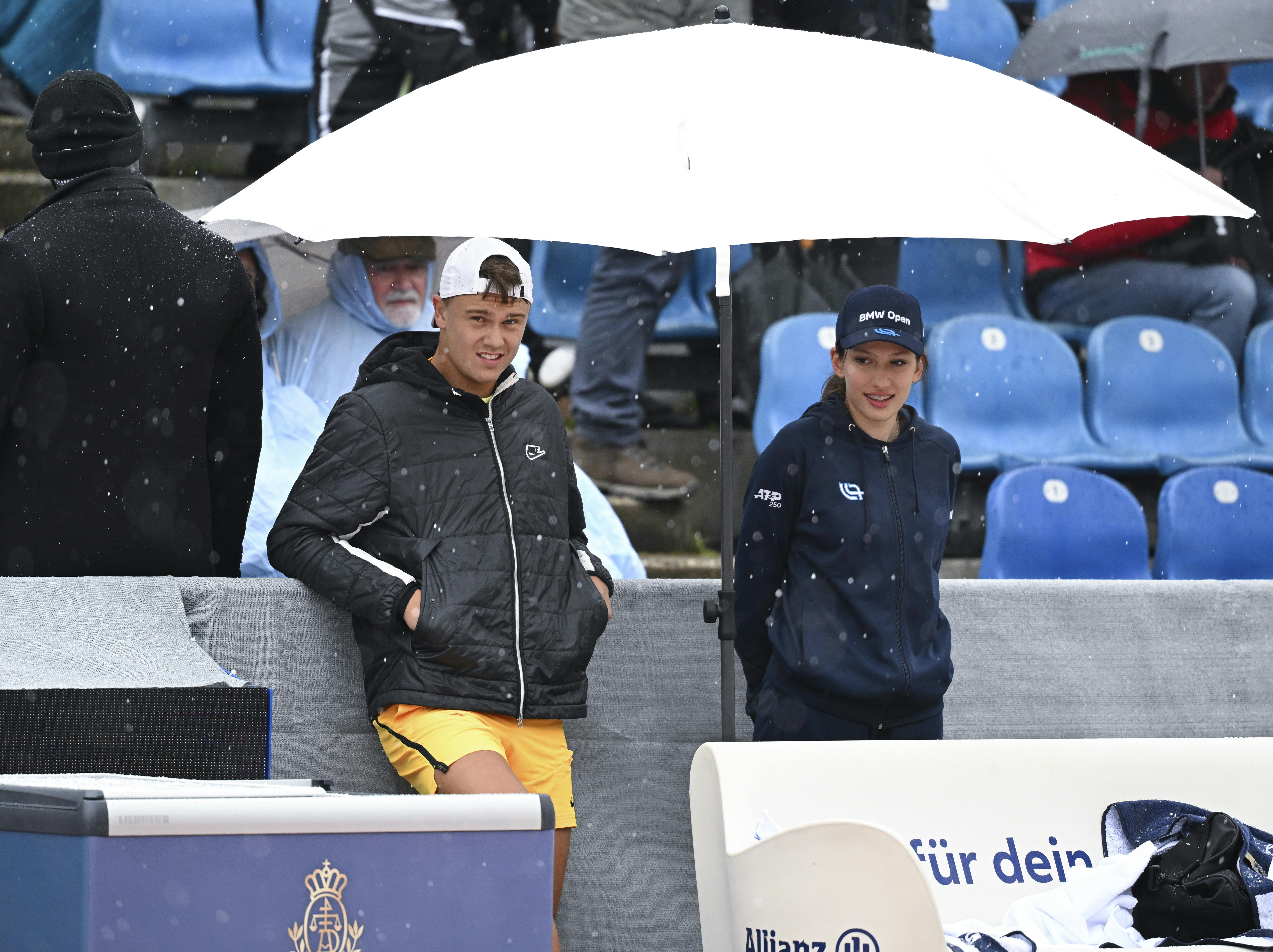 18 April 2024, Bavaria, Munich: Tennis: ATP Tour - Munich, Singles, Men, Round of 16. Rune (Denmark) - Galan (Colombia). Holger Rune (l) waits under an umbrella. The match was interrupted due to rain. Photo by: Sven Hoppe/picture-alliance/dpa/AP Images
