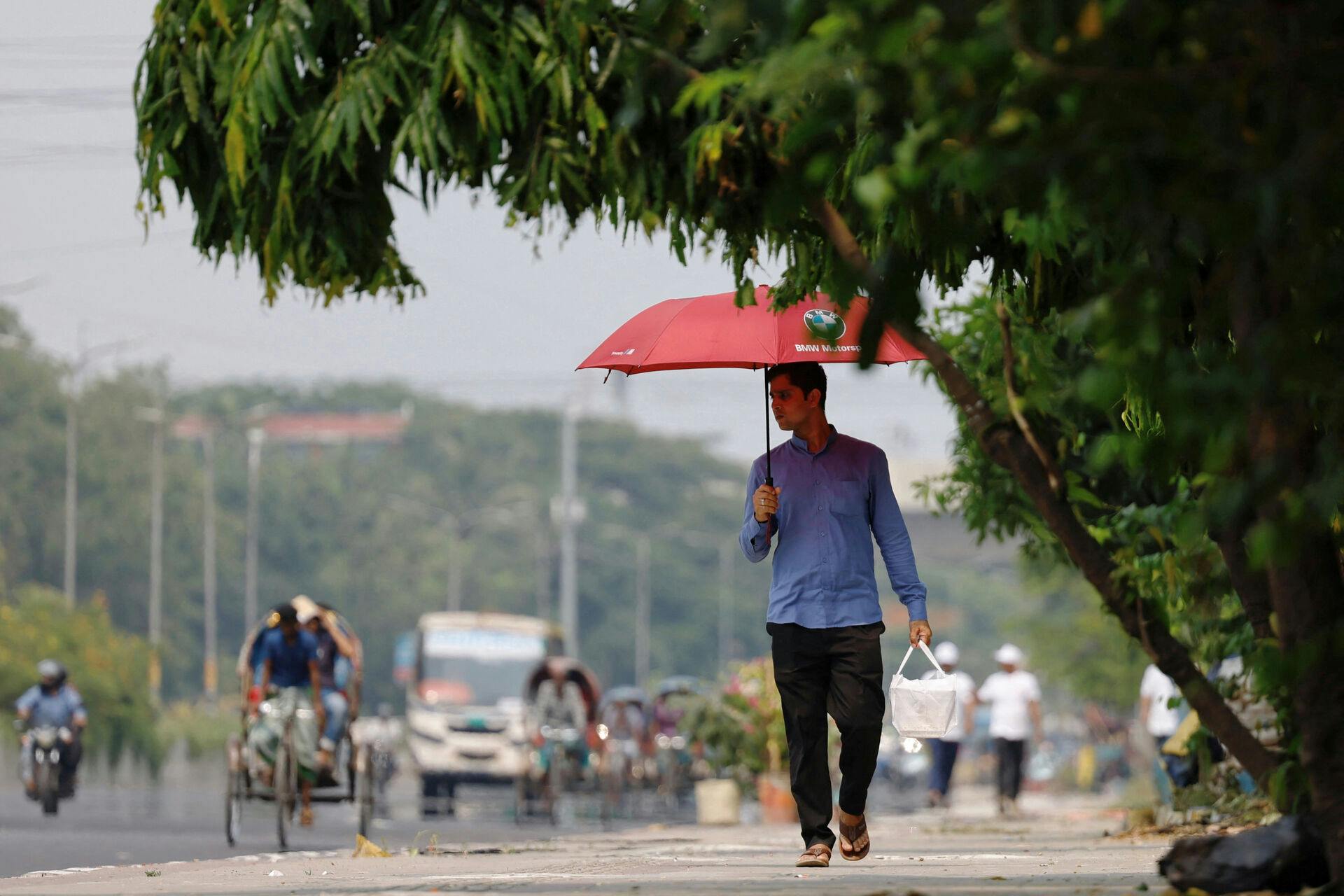 A man walks along a road with an umbrella to cover himself from the sun during a countrywide heatwave in Dhaka, Bangladesh, April 28, 2024. REUTERS/Mohammad Ponir Hossain