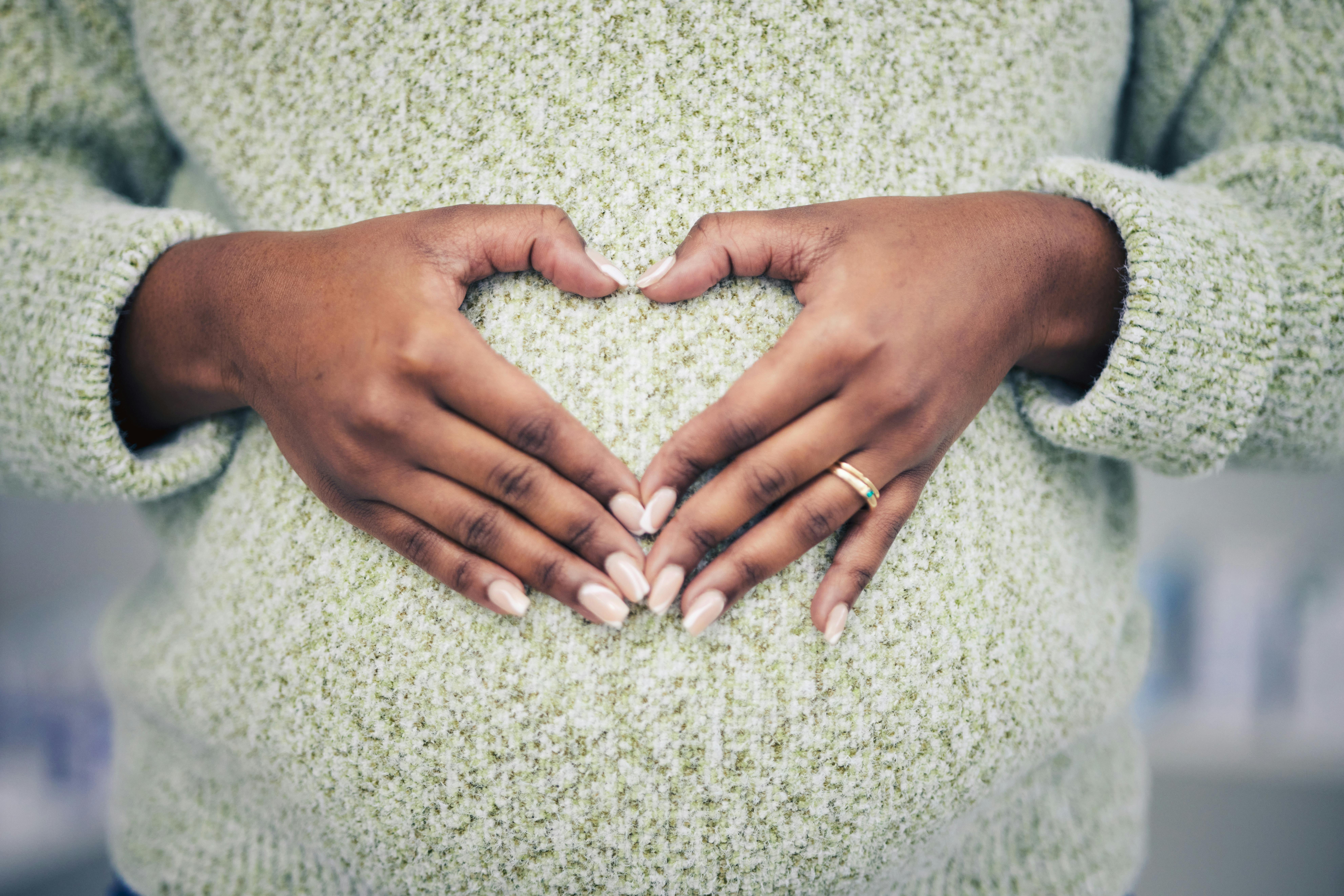 Pregnancy, closeup and woman with a heart shape on her maternal belly for care and motherhood. Health, zoom and African pregnant female person hands on stomach with a love sign or emoji for her baby