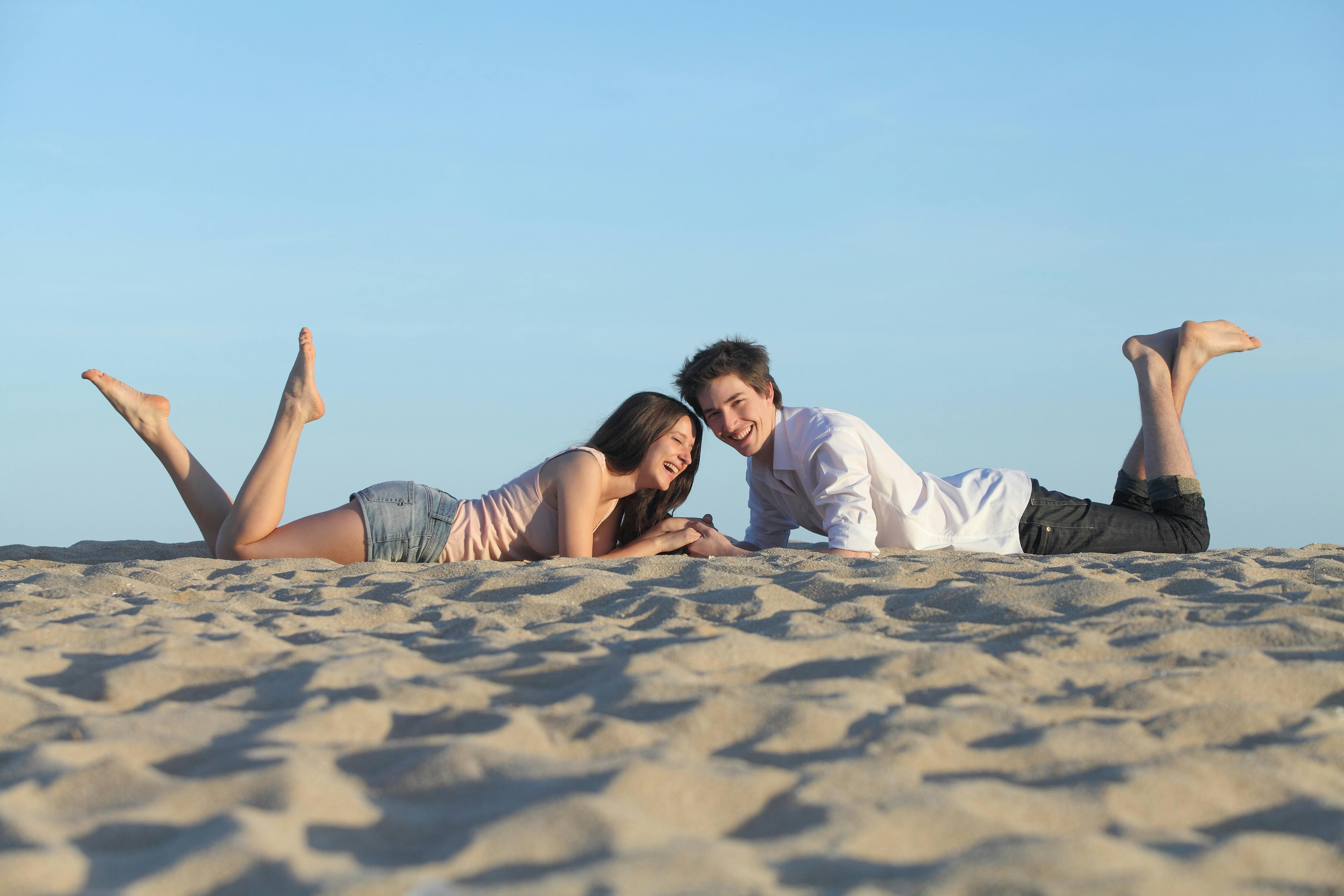 Couple laughing resting on the sand of a beach with the sky in the background