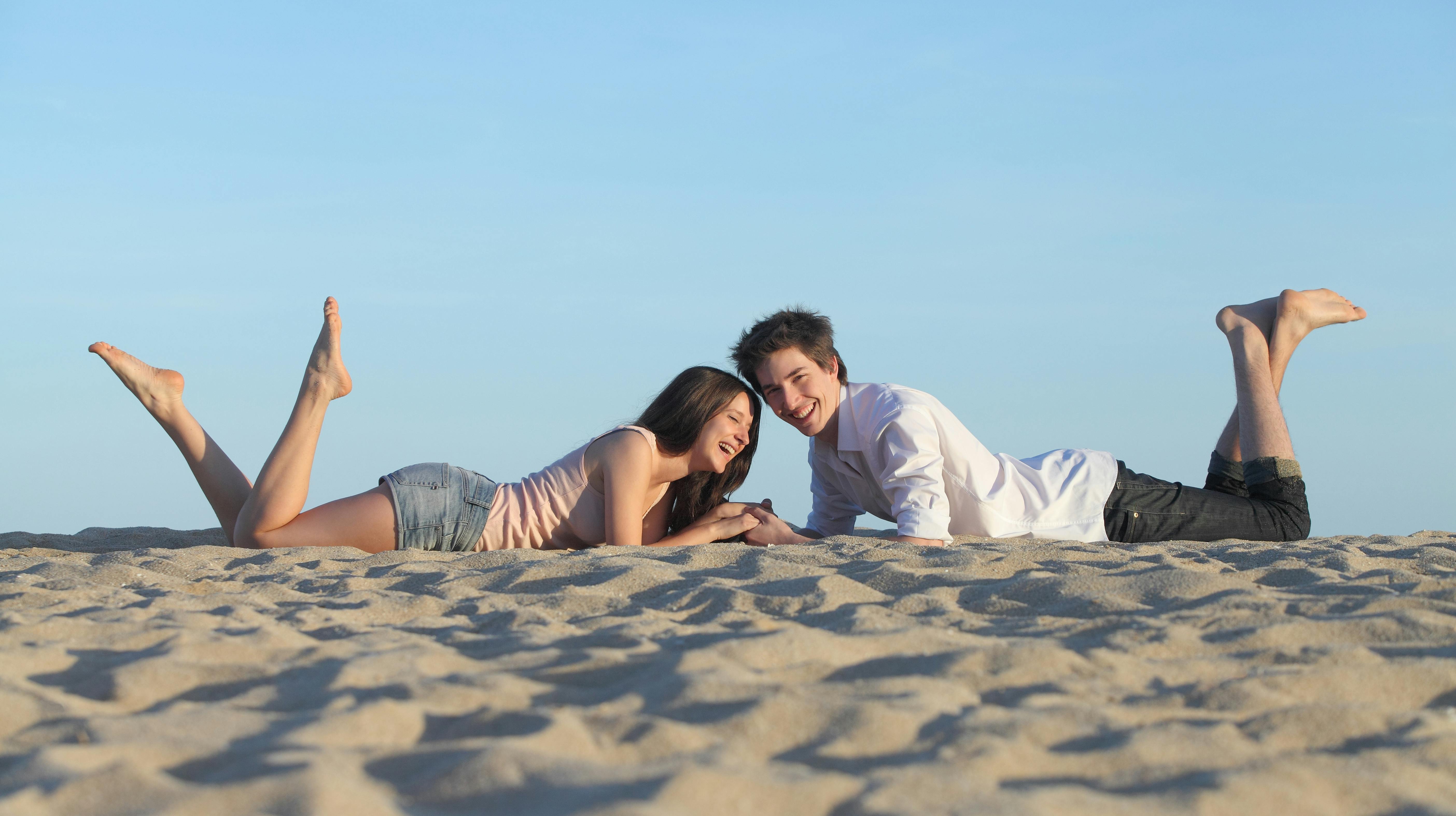Couple laughing resting on the sand of a beach with the sky in the background
