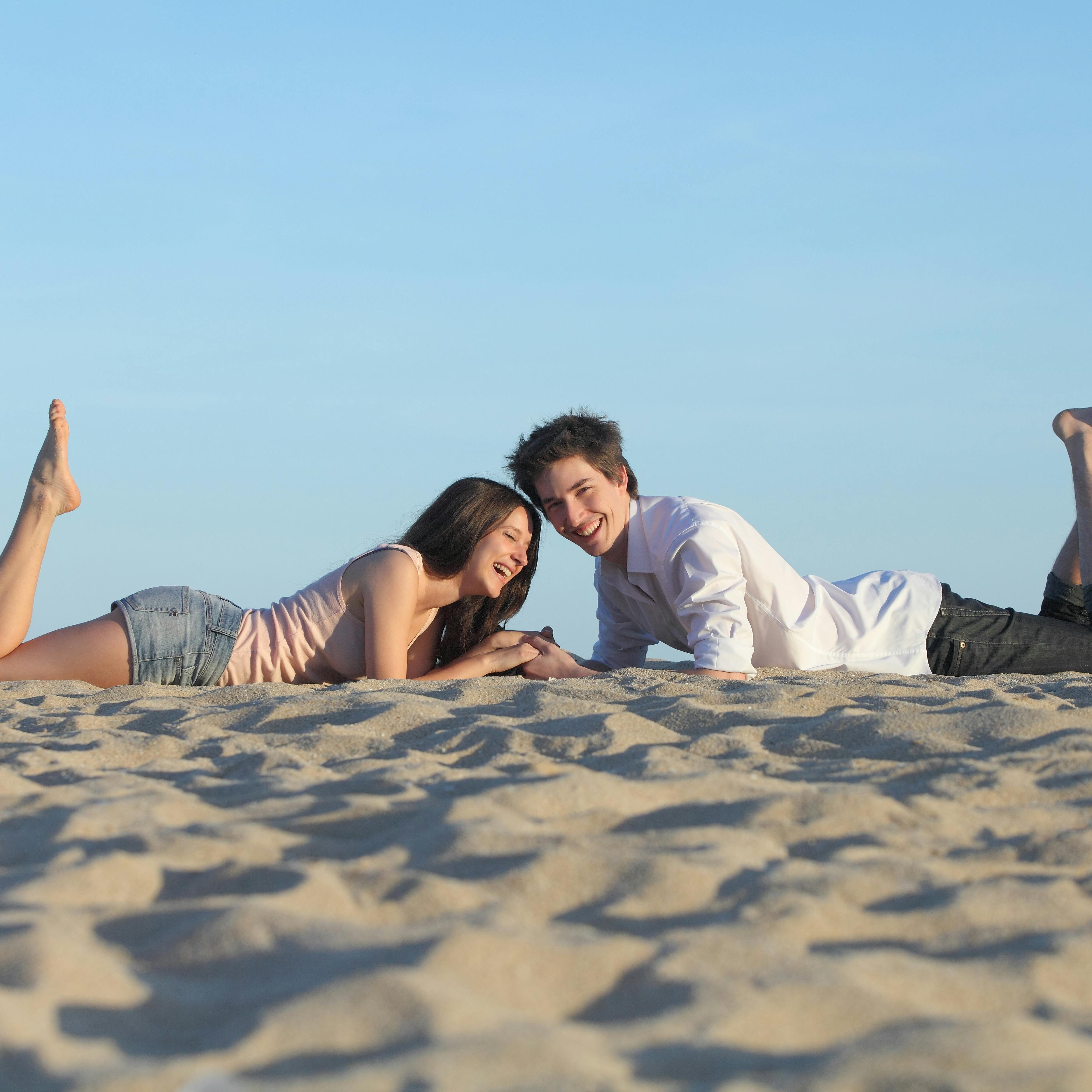 Couple laughing resting on the sand of a beach with the sky in the background