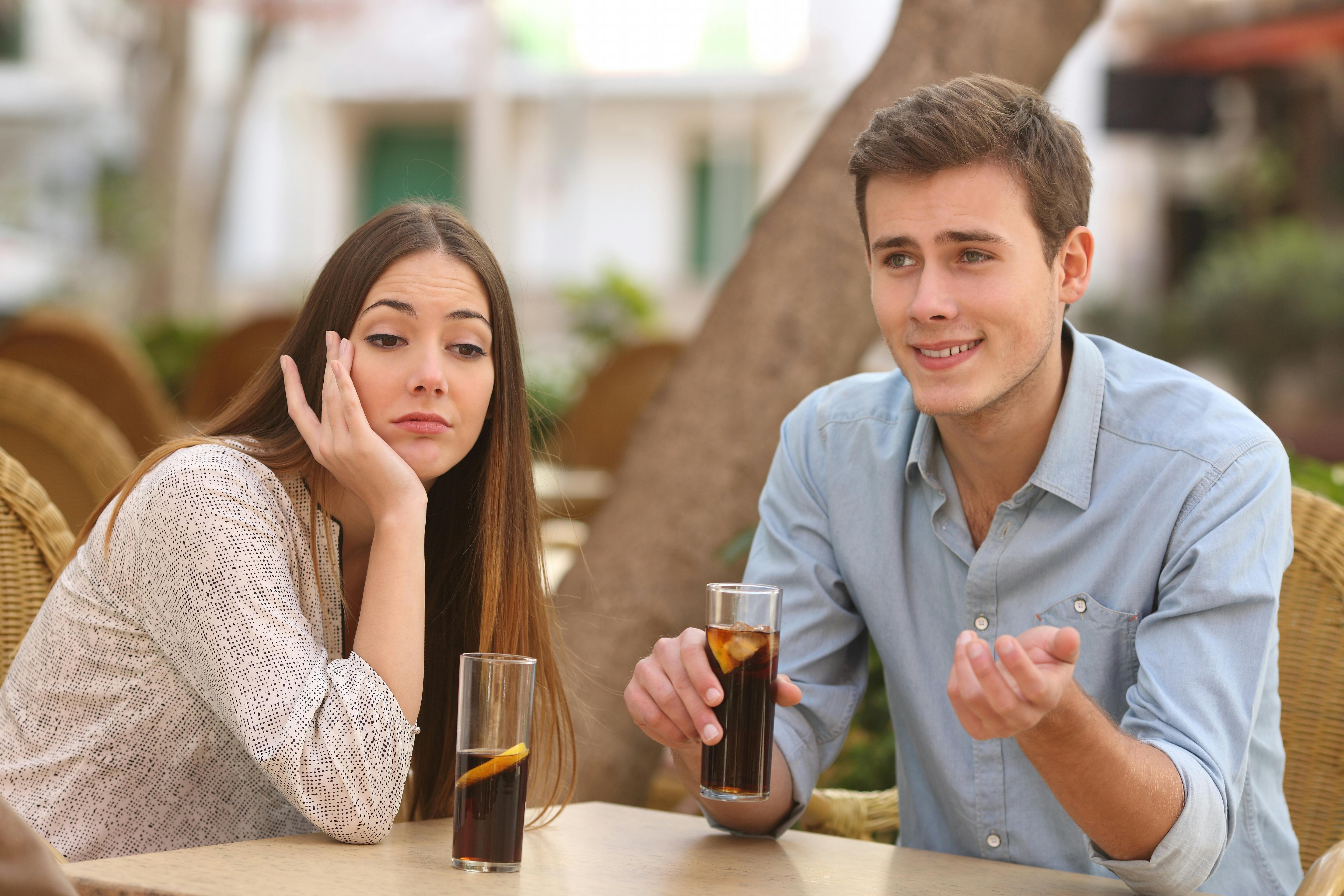 Man and woman dating in a restaurant terrace but she is boring while he speaks