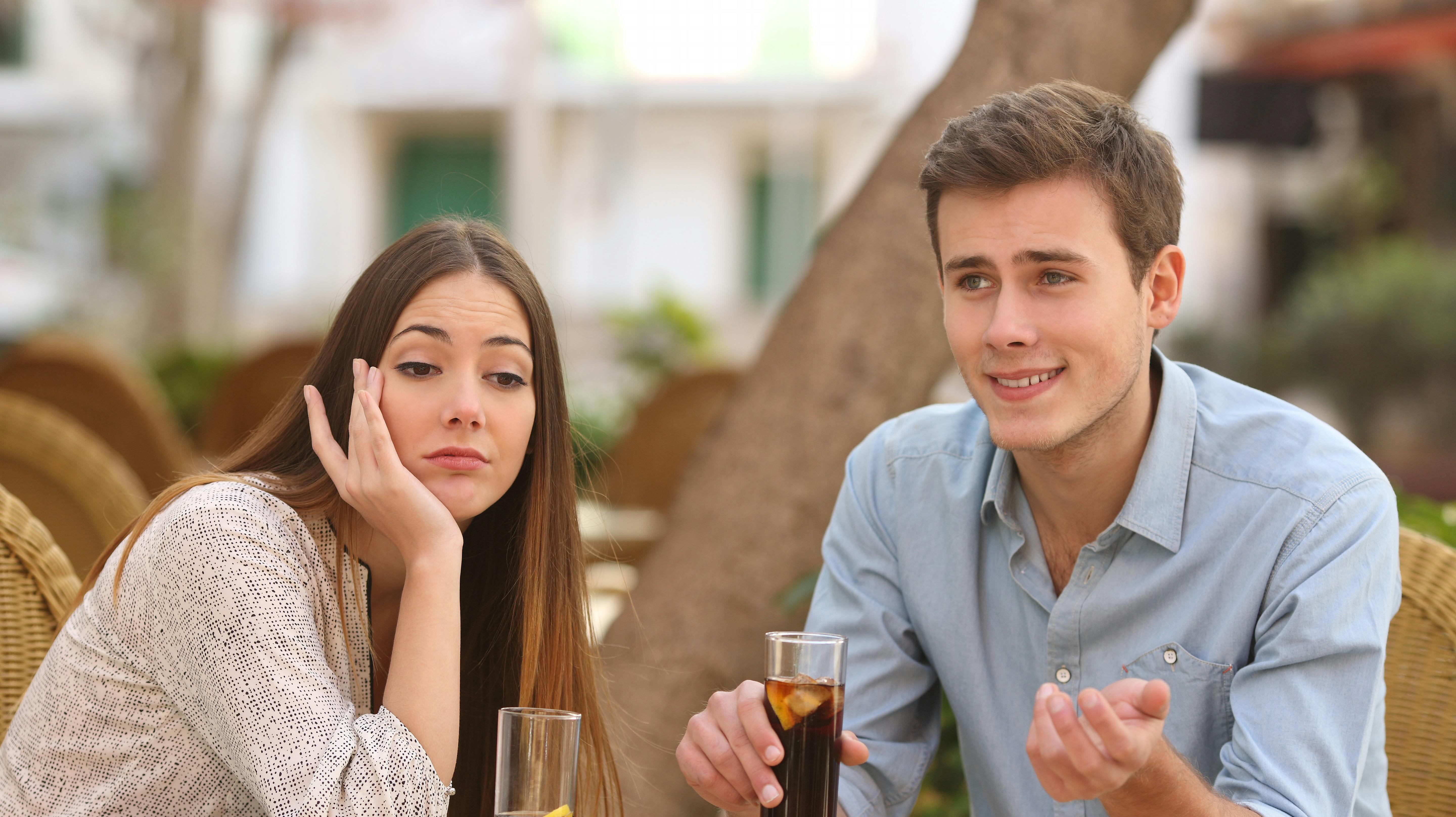 Man and woman dating in a restaurant terrace but she is boring while he speaks