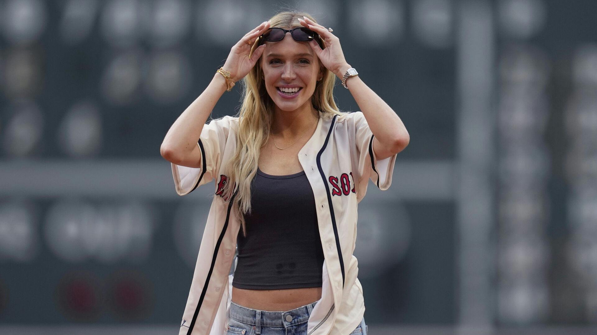 Social media influencer and podcaster Alex Cooper adjusts her sunglasses while preparing to deliver the ceremonial first pitch at Fenway Park, Wednesday, June 26, 2024, in Boston. (AP Photo/Charles Krupa)