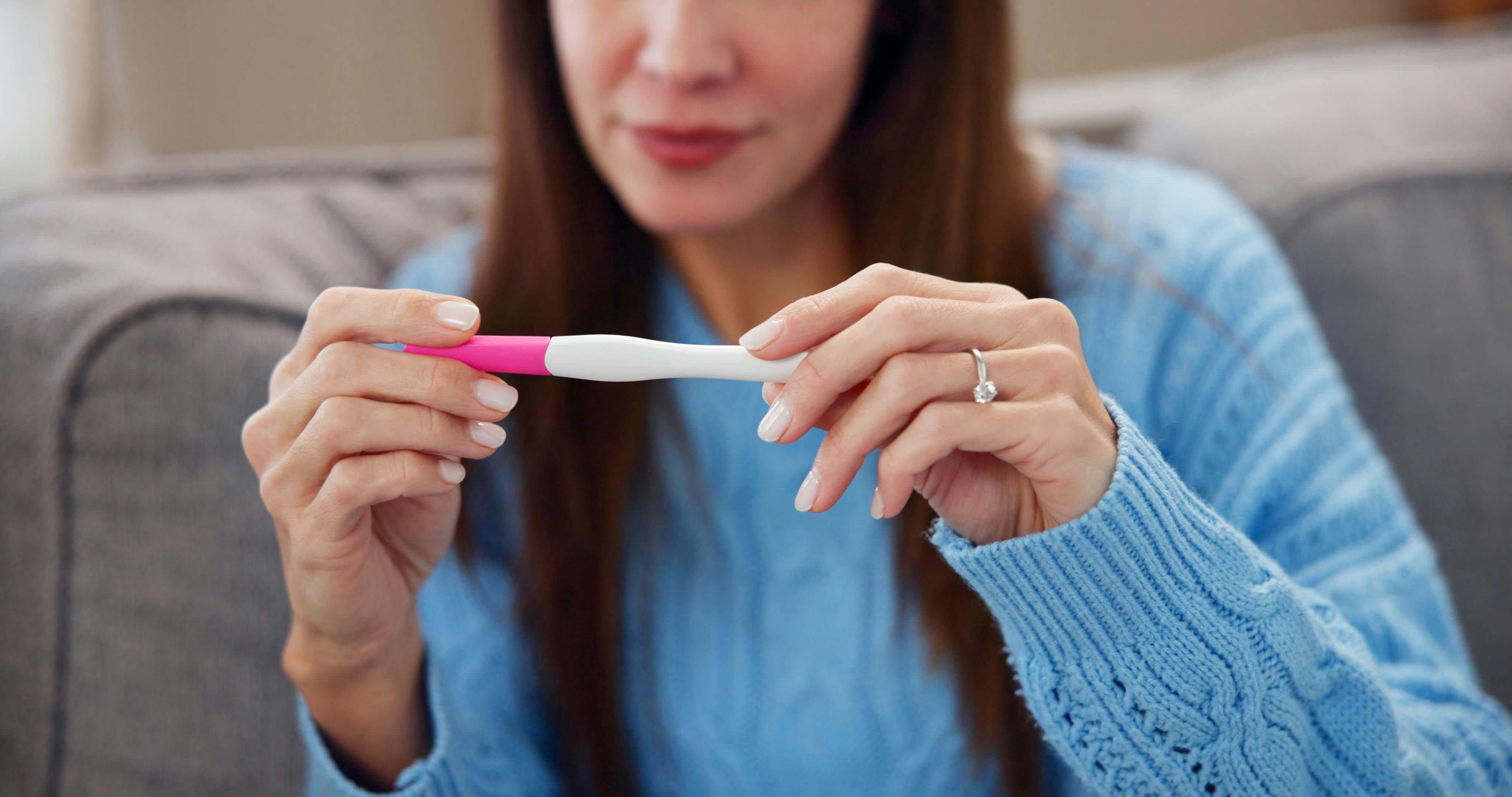 Pregnancy test, results and hands of woman on sofa for fertility treatment, ivf and family planning. Home, pregnant and person with medical stick for news, maternity or health on couch in living room.