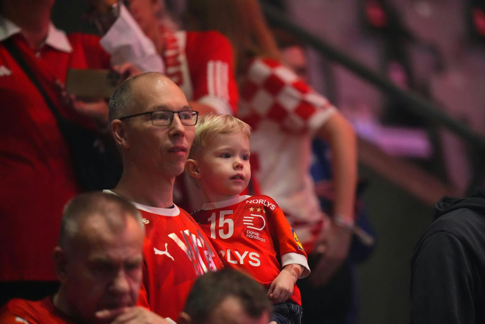 Store som små i rødt - kom så Danmark! Her er det Sigurd, som sidder på armen af sin farfar Jesper, mens far og søn Magnus Saugstrup spiller.