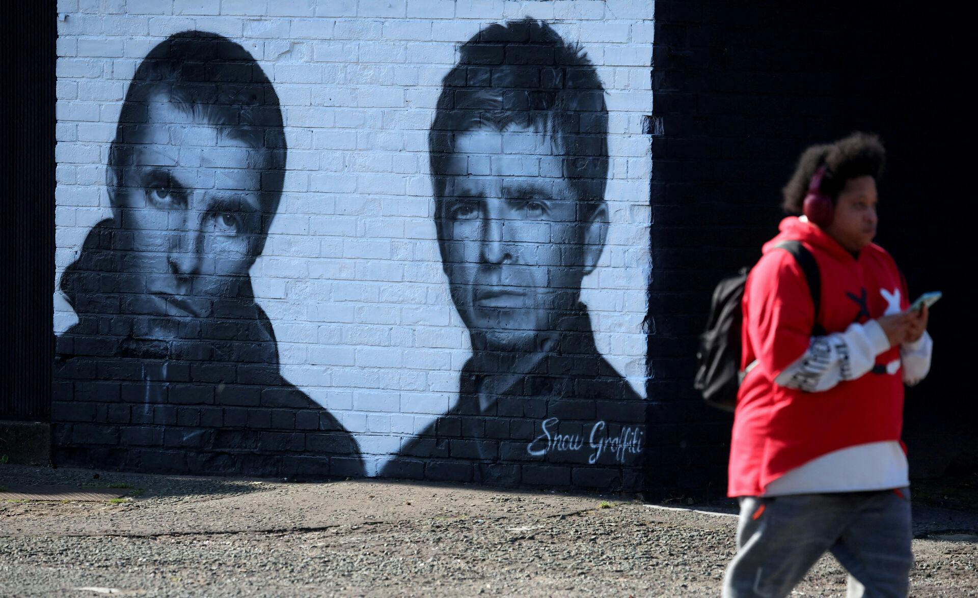 FILE PHOTO: A man walks past a mural of Oasis band members Liam and Noel Gallagher by artist Snow Graffiti on the wall of the Coach and Horses pub in Whitefield, near Manchester, Britain, August 31, 2024. REUTERS/Phil Noble/File Photo