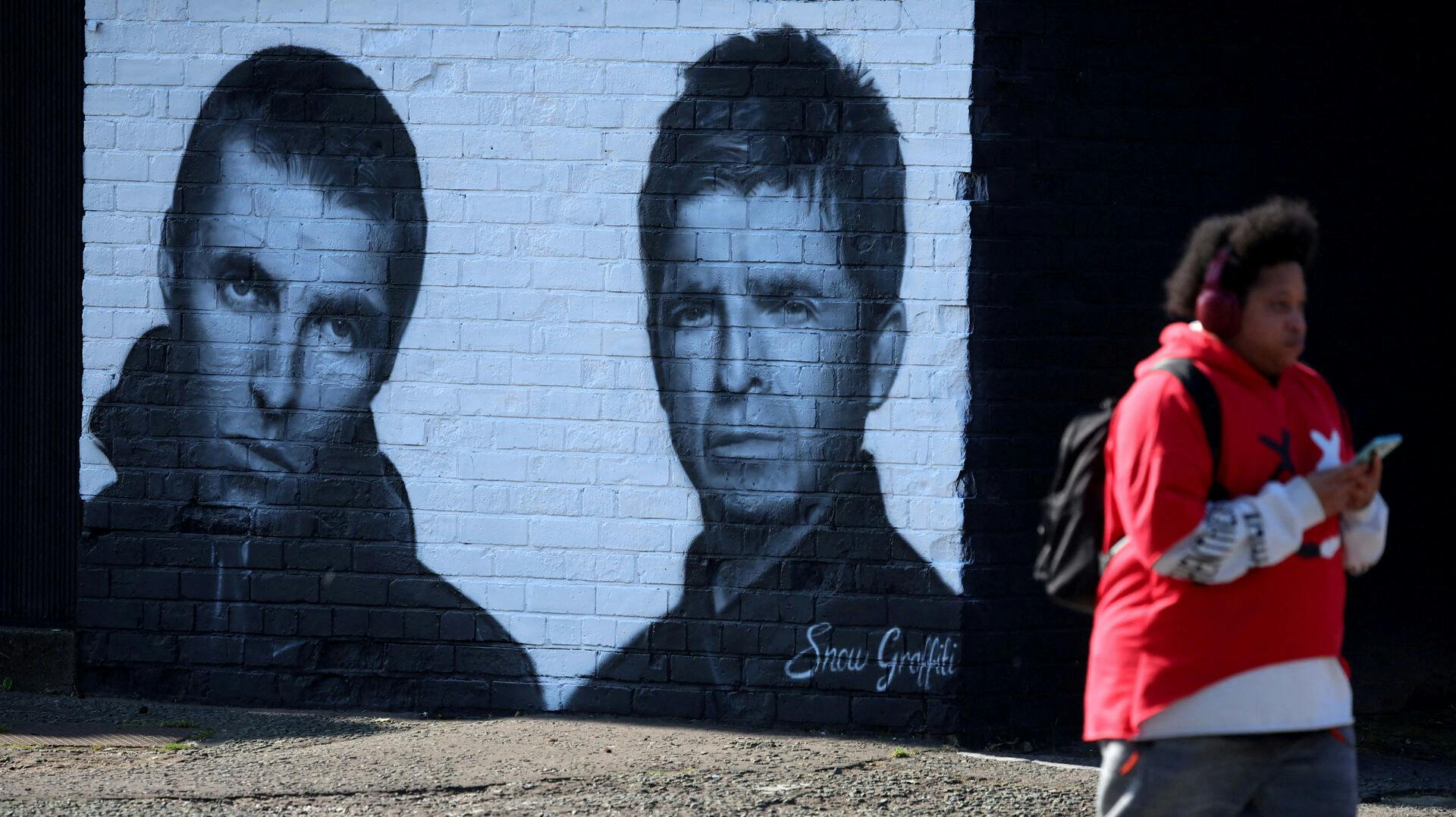 FILE PHOTO: A man walks past a mural of Oasis band members Liam and Noel Gallagher by artist Snow Graffiti on the wall of the Coach and Horses pub in Whitefield, near Manchester, Britain, August 31, 2024. REUTERS/Phil Noble/File Photo