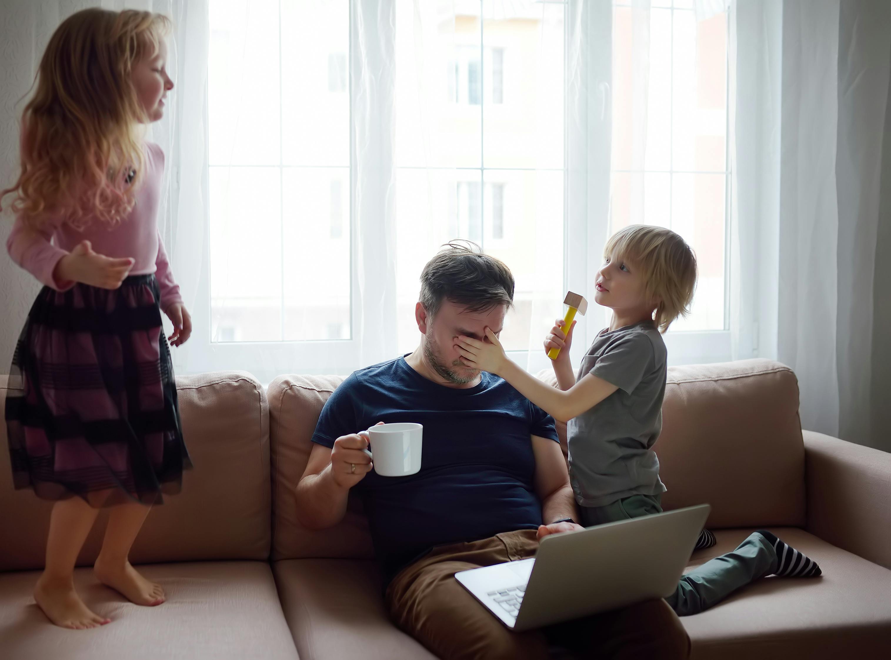 Tired father with his two kids during quarantine. Stay at home concept. Online working and household at the same time while quarantine. Exhausted parents with children.
