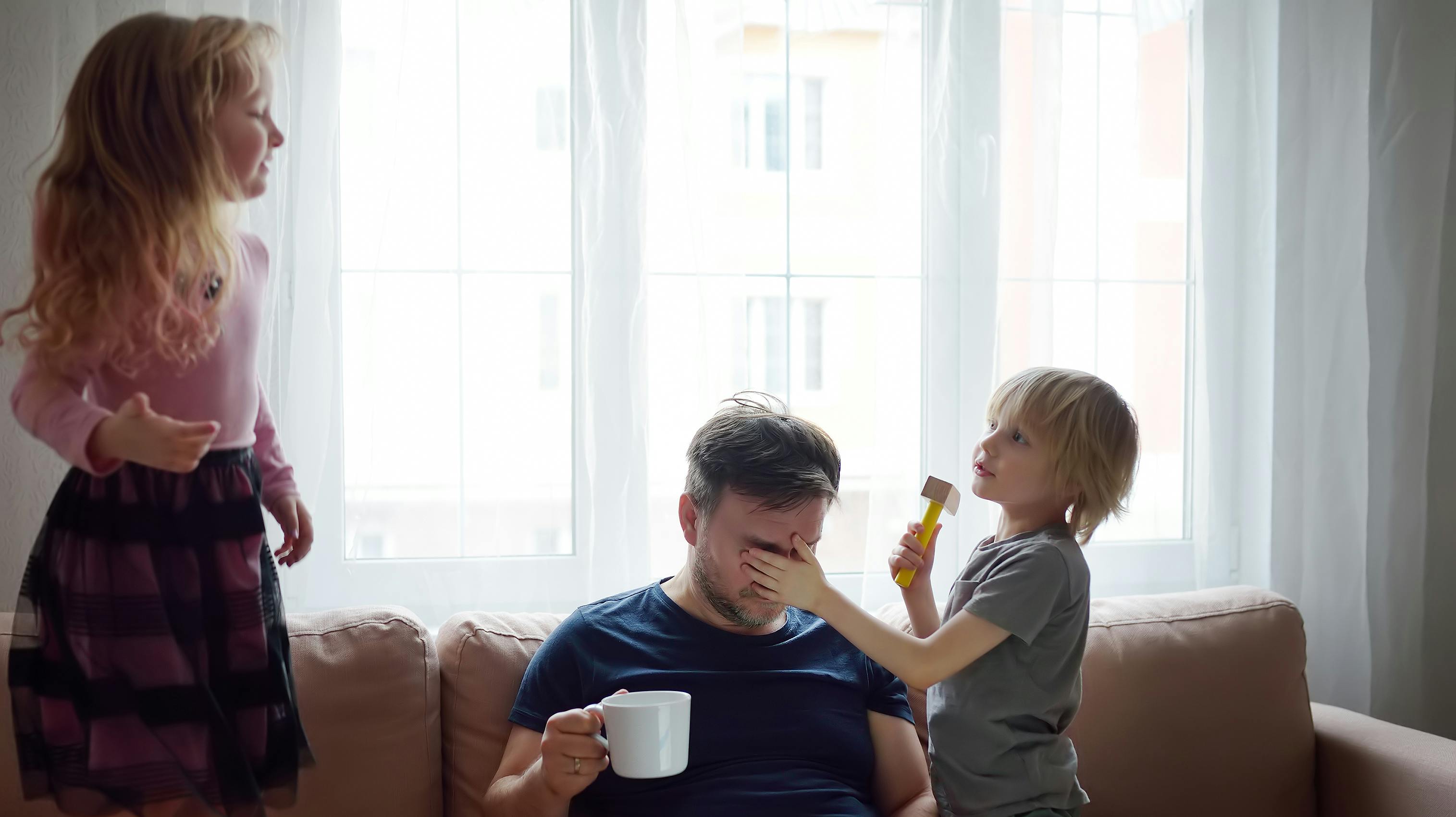 Tired father with his two kids during quarantine. Stay at home concept. Online working and household at the same time while quarantine. Exhausted parents with children.