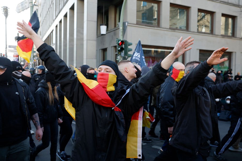 En ung mand deltager i en nynazistisk demonstration i Berlin. Han har viklet Tysklands flag om sine skuldre og rækker begge arme op. - Foto: Odd Andersen/Ritzau Scanpix