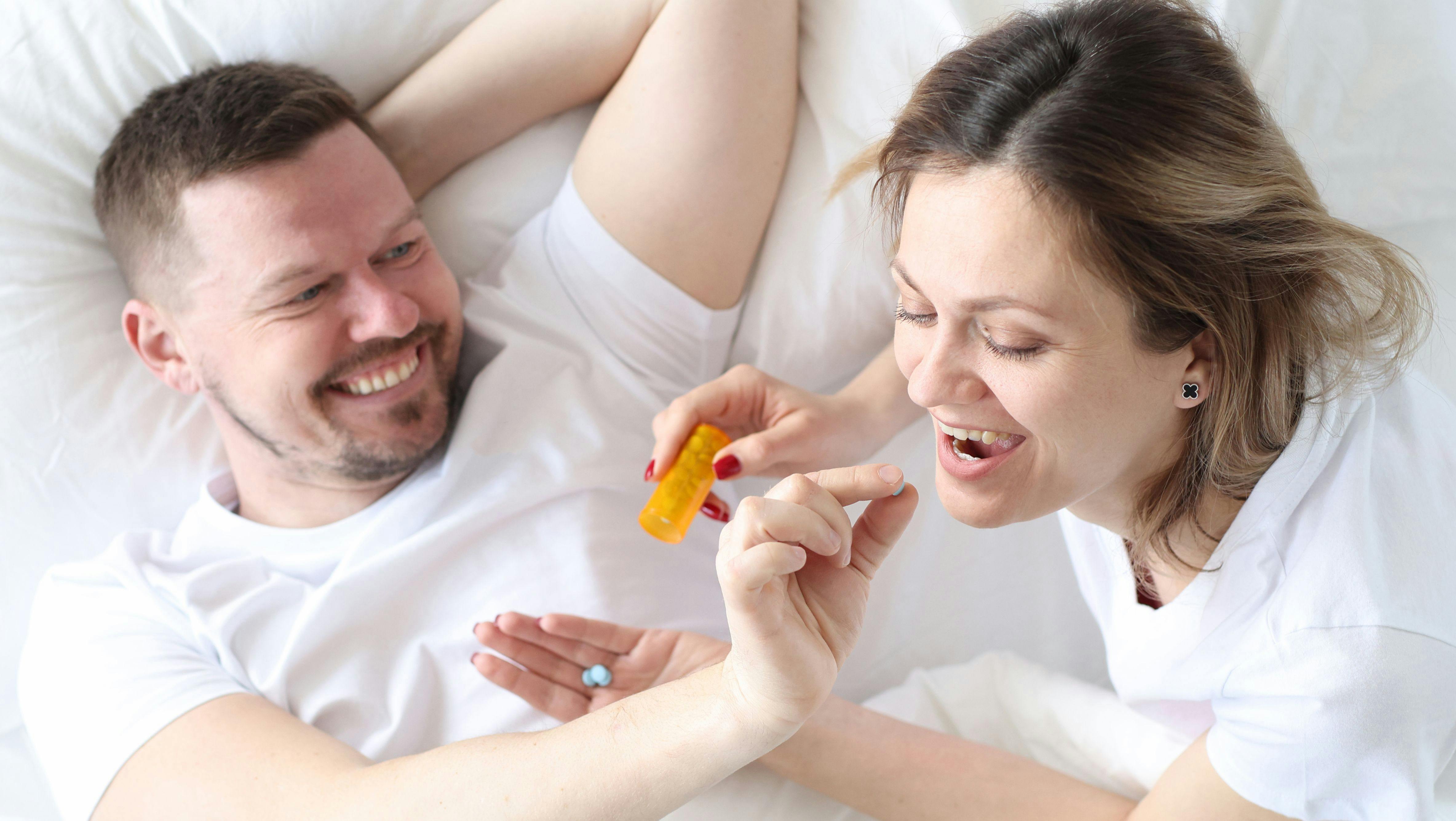 Man gives woman a birth control pill on bed. Safe sex concept
