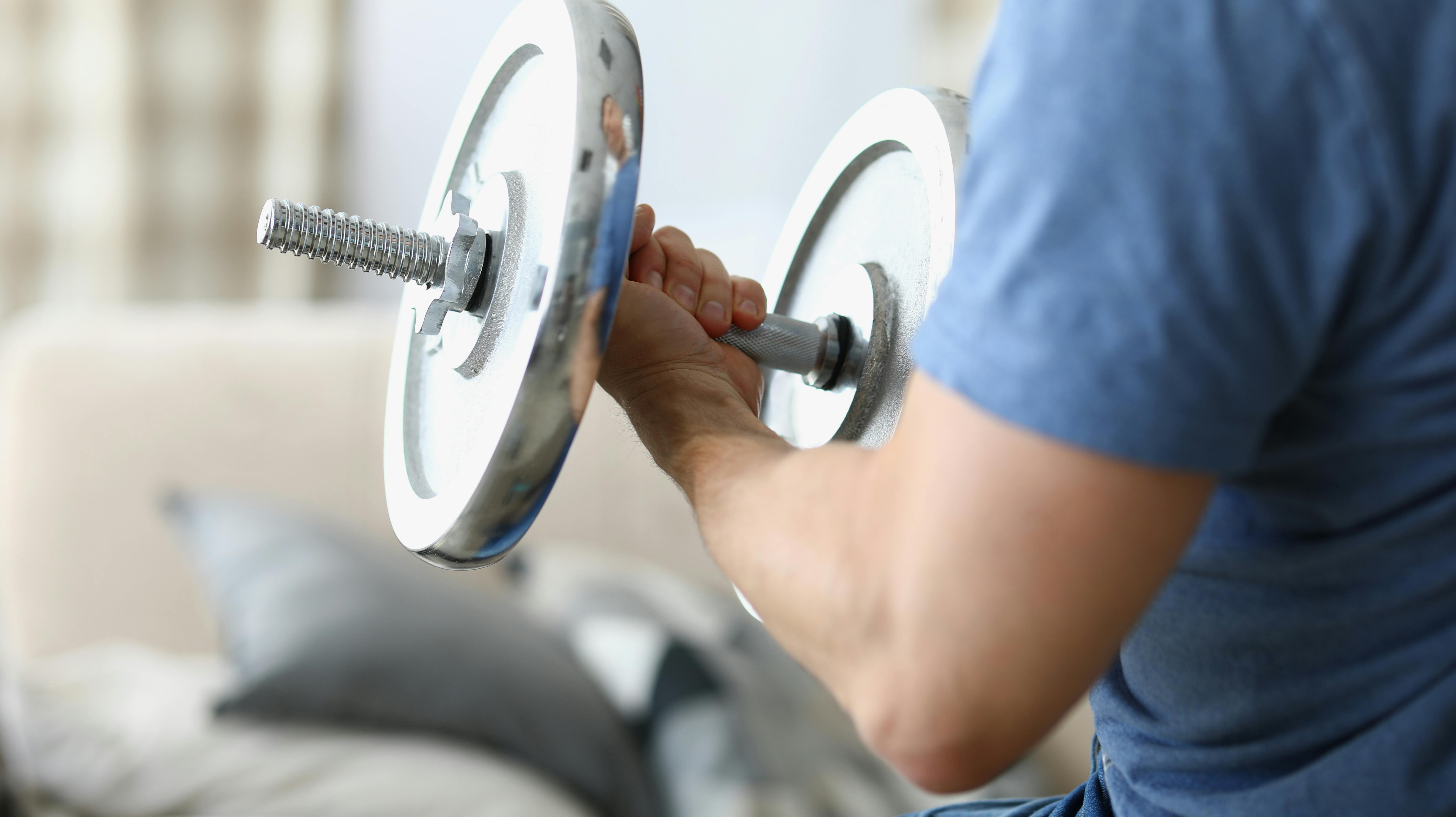 Man hand lifts heavy dumbbell while swinging biceps. Exercises for strong biceps concept