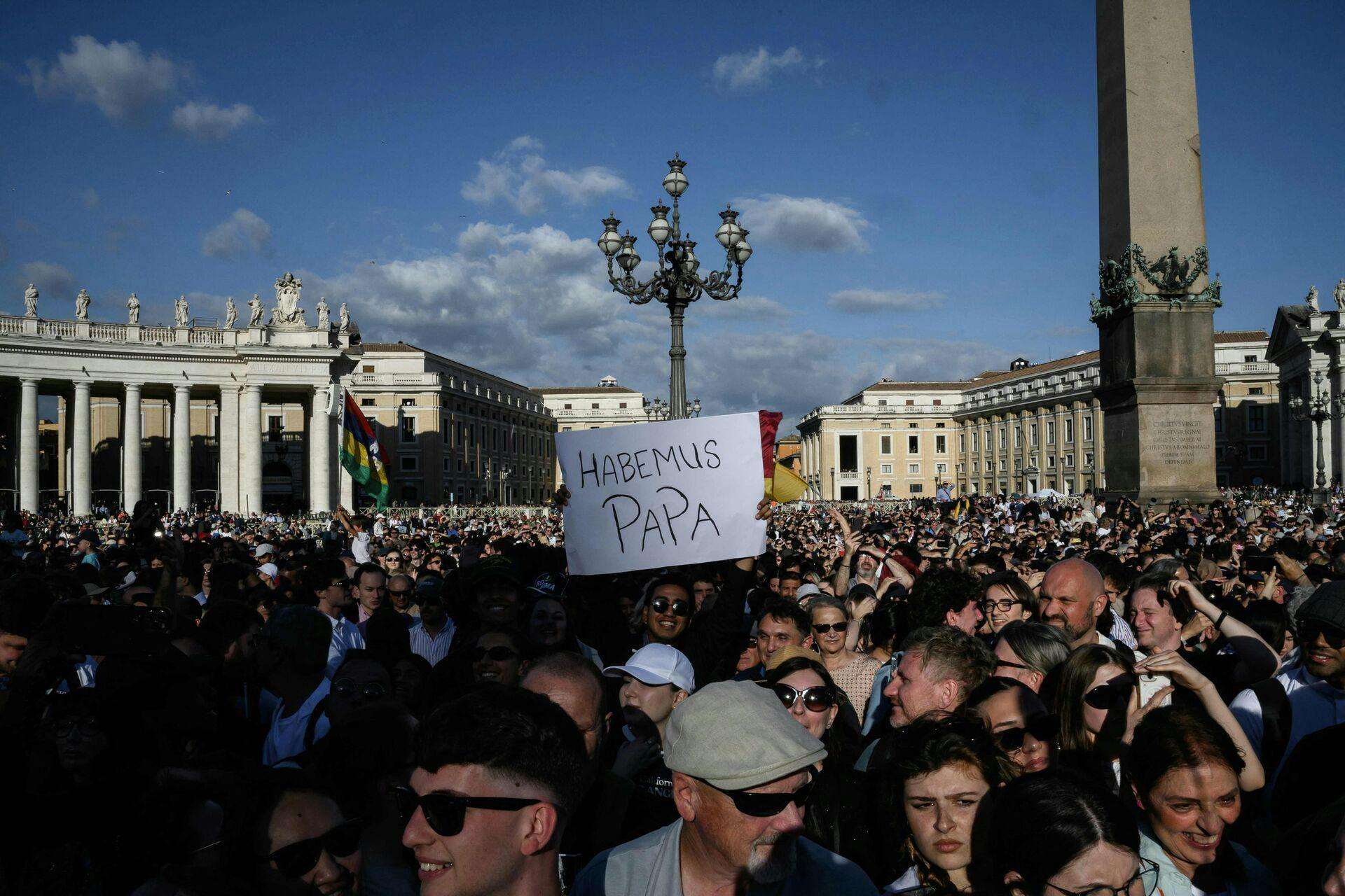 TOPSHOT - A man holds a placard reading "Habemus Papa" (We Have a Pope) after white smoke rose from the chimney of the Sistine Chapel signalling that cardinals elected a new pope during their secret conclave, at Saint Peter's Square in The Vatican, on May 8, 2025. Thick black smoke billowed on May 8, 2025, from the chimney of the Sistine Chapel in a sign that cardinals again failed to elect a new head of the Catholic Church. (Photo by JEFF PACHOUD / AFP)