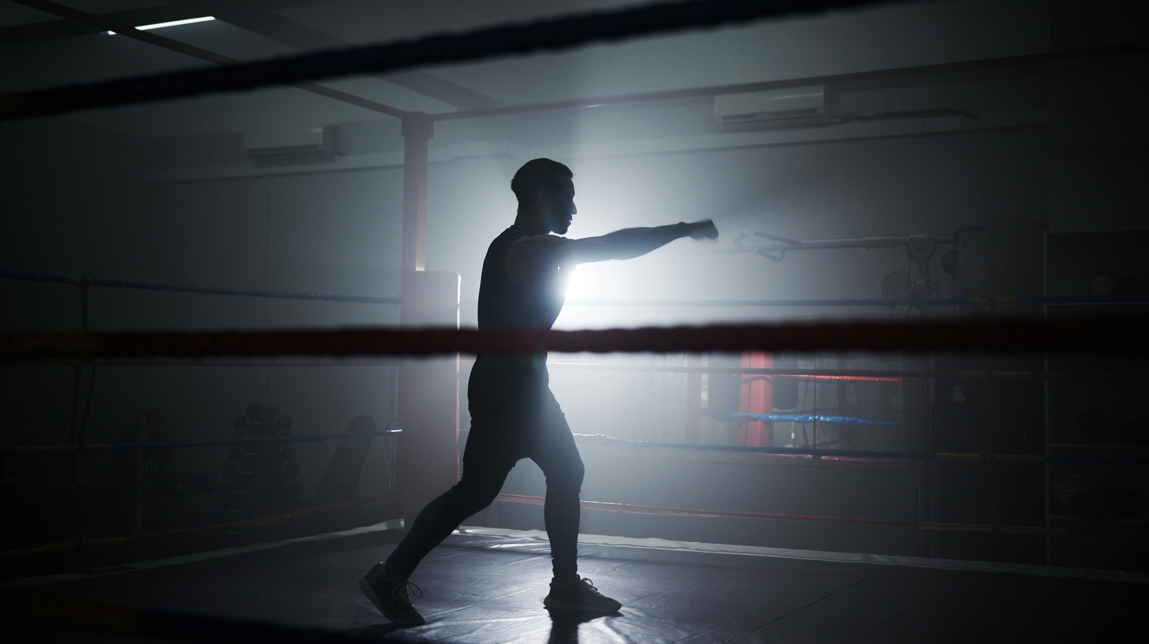 Boxing, punch and silhouette with man in ring for sparring practice, training and fitness. Mma club, wrestling challenge and martial arts fighter with person in gym for performance and self defense.