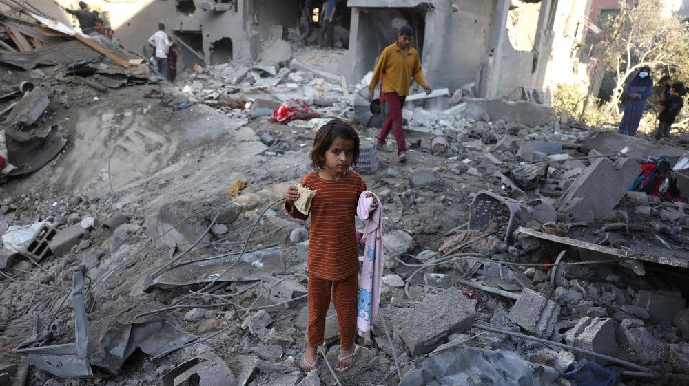 En pige spiser en skive brød, mens andre palæstinensere omkring hende besigtiger skaderne efter et nyt israelsk angreb i Jabalia i den centrale del af Gazastriben fredag.