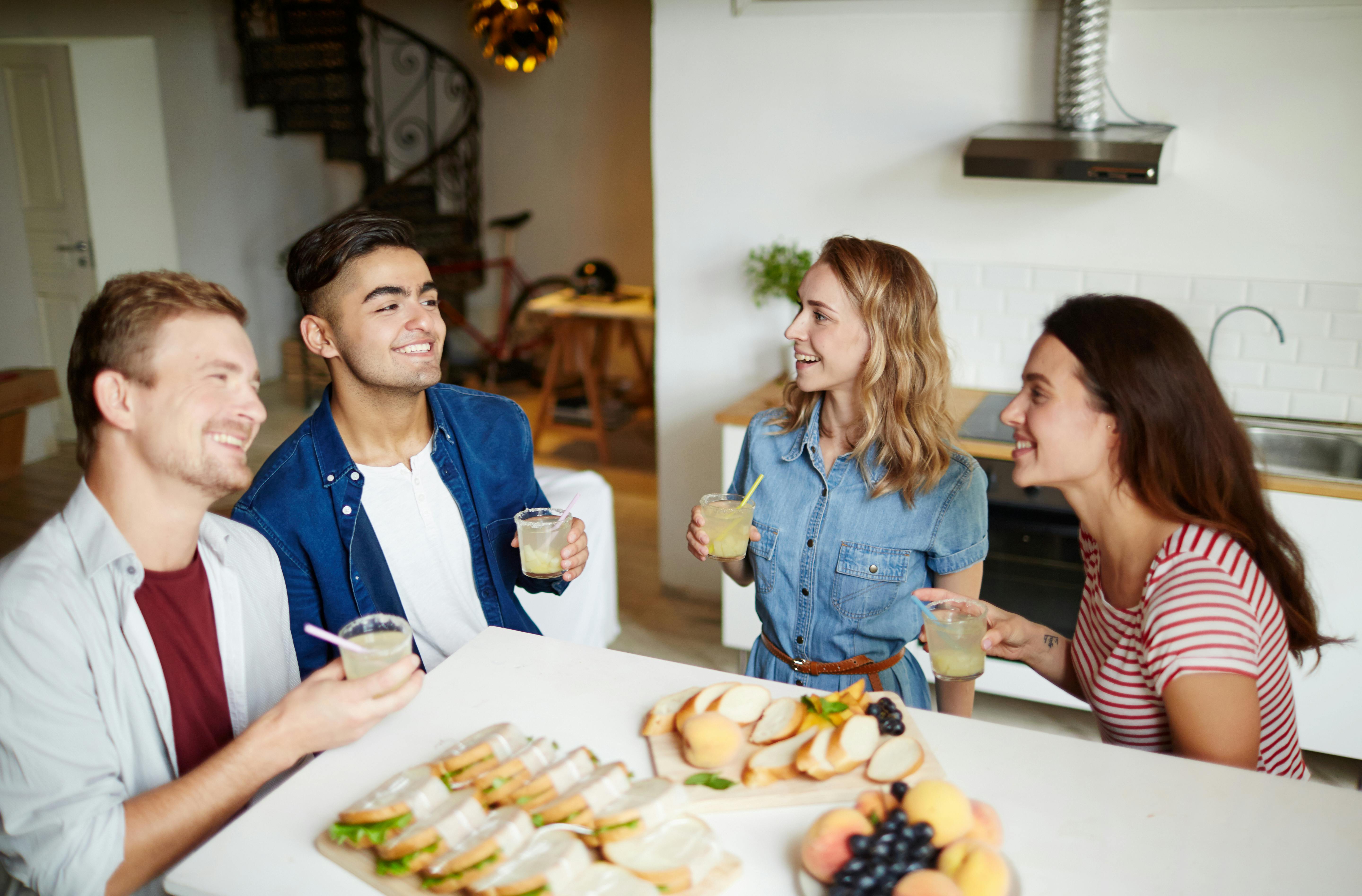 Two guys and their girlfriends holding drinks and enjoying talk at home on Friday evening