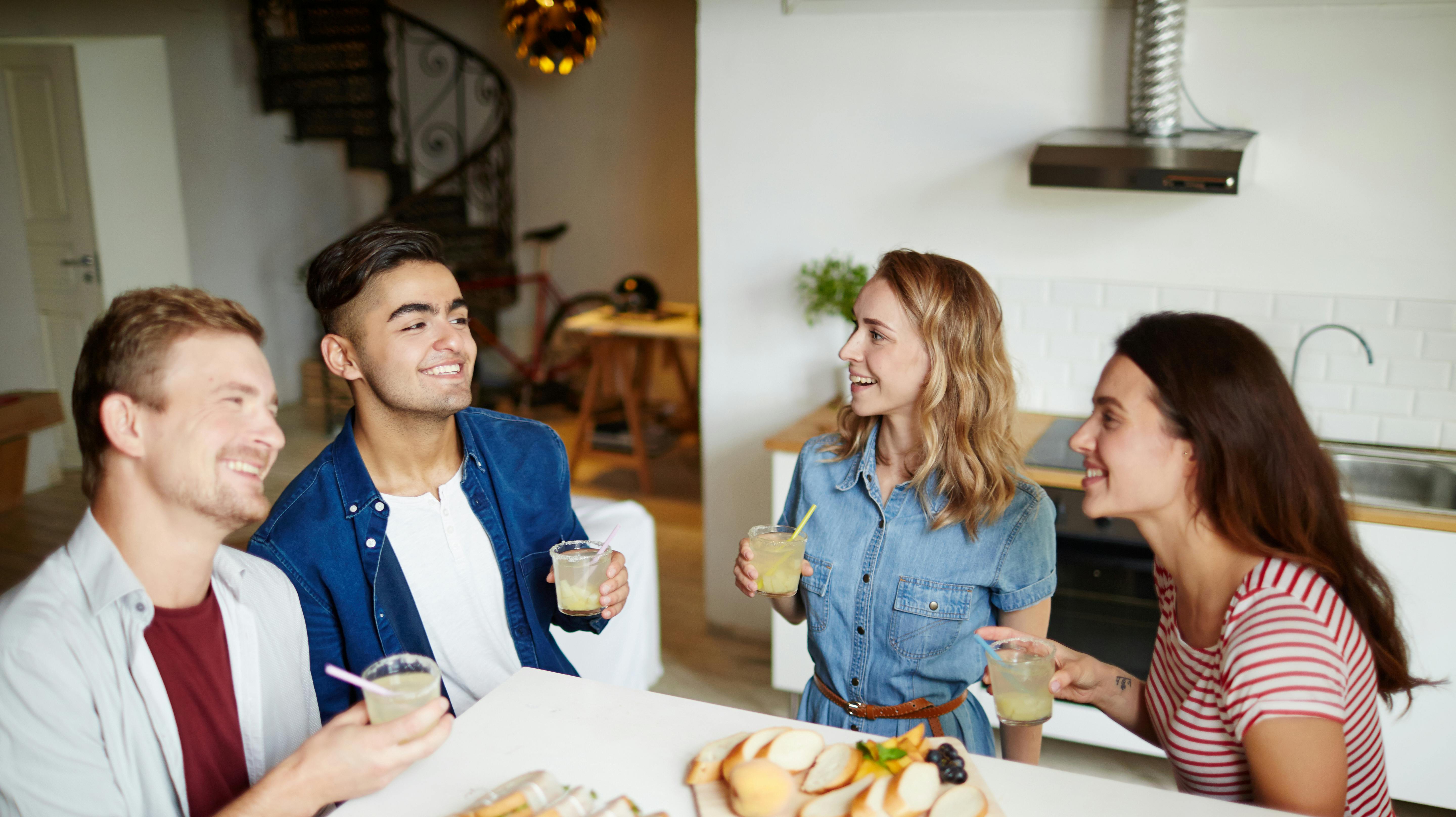 Two guys and their girlfriends holding drinks and enjoying talk at home on Friday evening