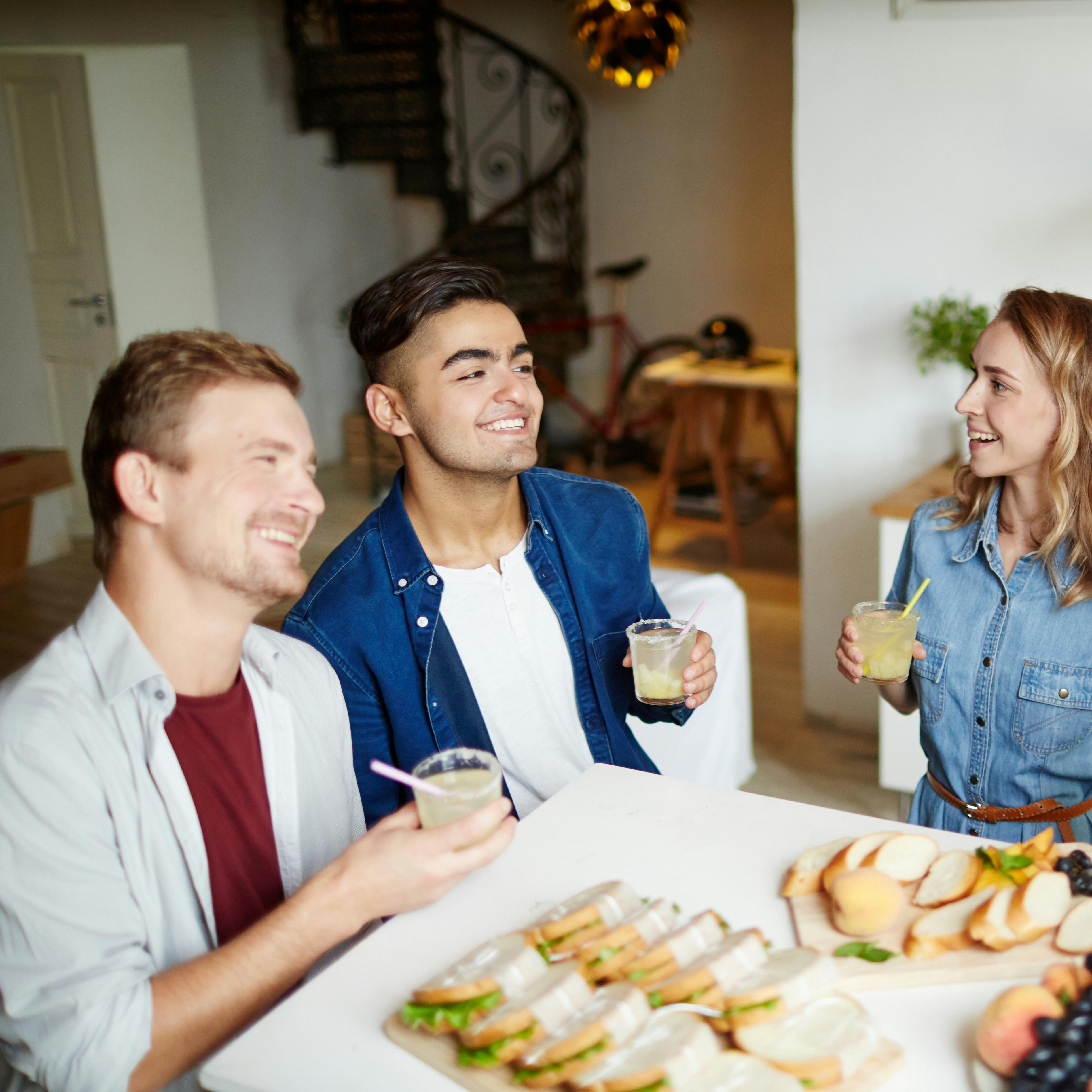 Two guys and their girlfriends holding drinks and enjoying talk at home on Friday evening