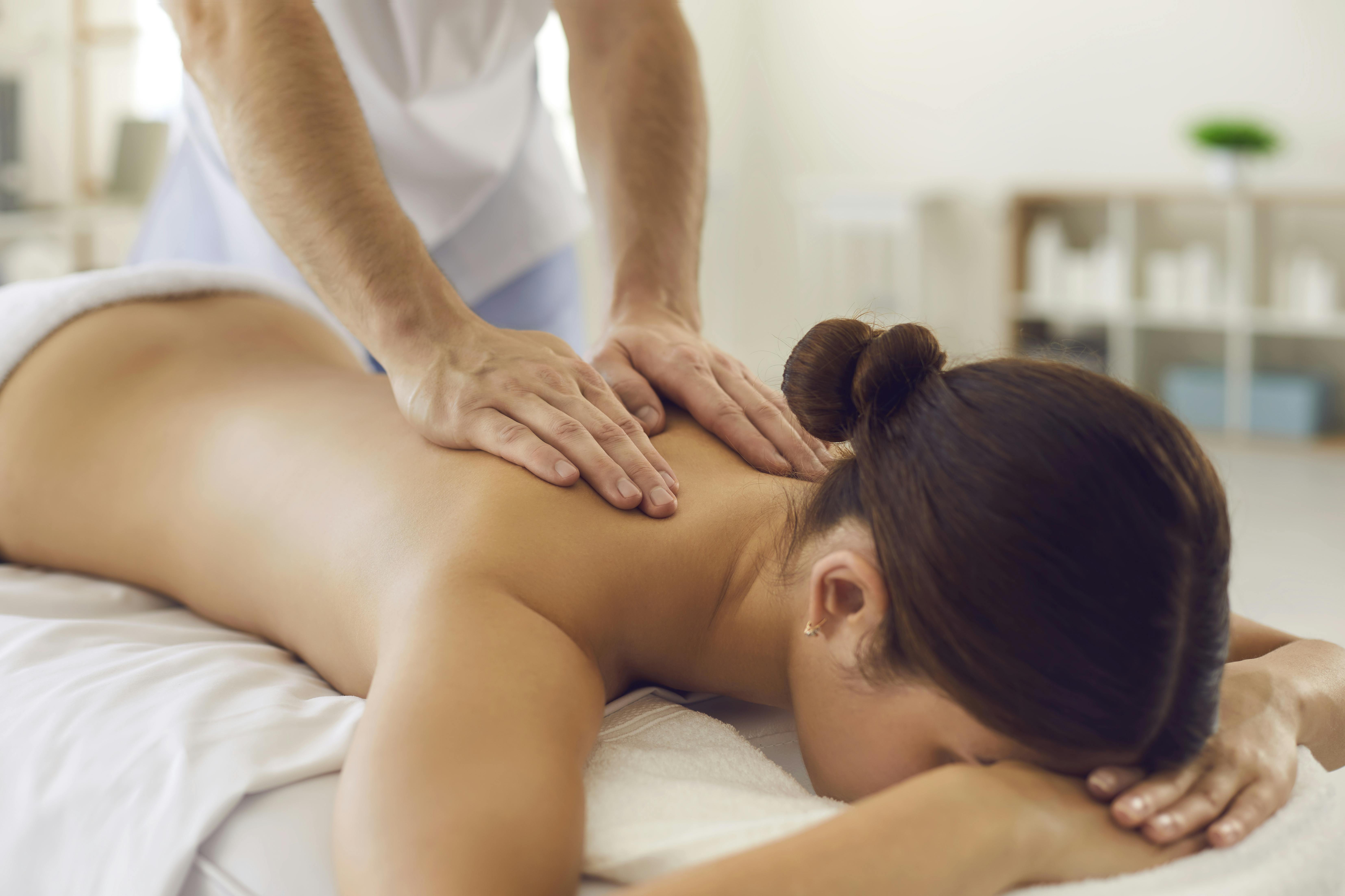 Faceless brunette woman lies on the couch and receives a massage of the neck-collar area from a professional masseur. Hands of the massage therapist on the body of the patient close up.