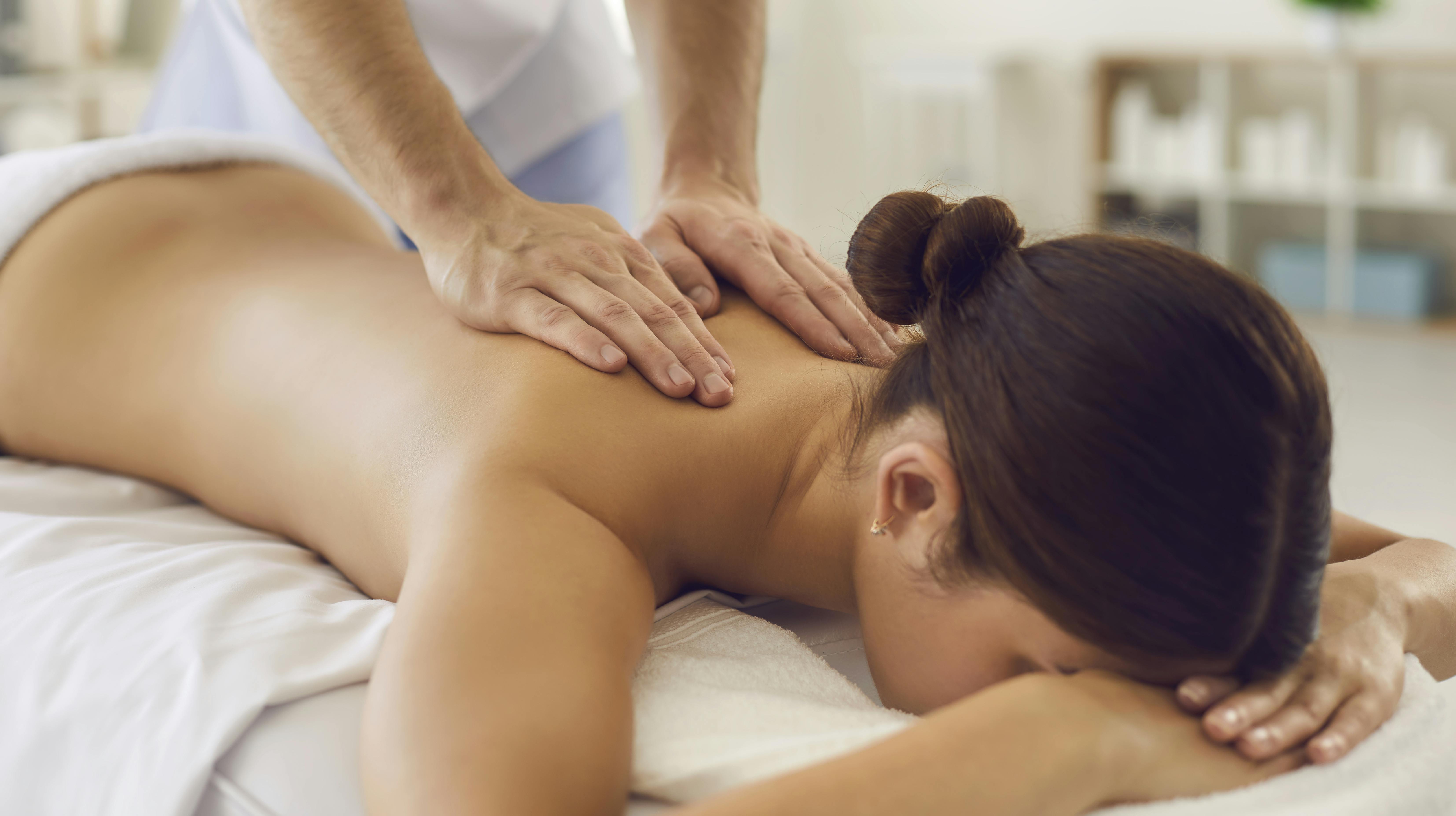 Faceless brunette woman lies on the couch and receives a massage of the neck-collar area from a professional masseur. Hands of the massage therapist on the body of the patient close up.