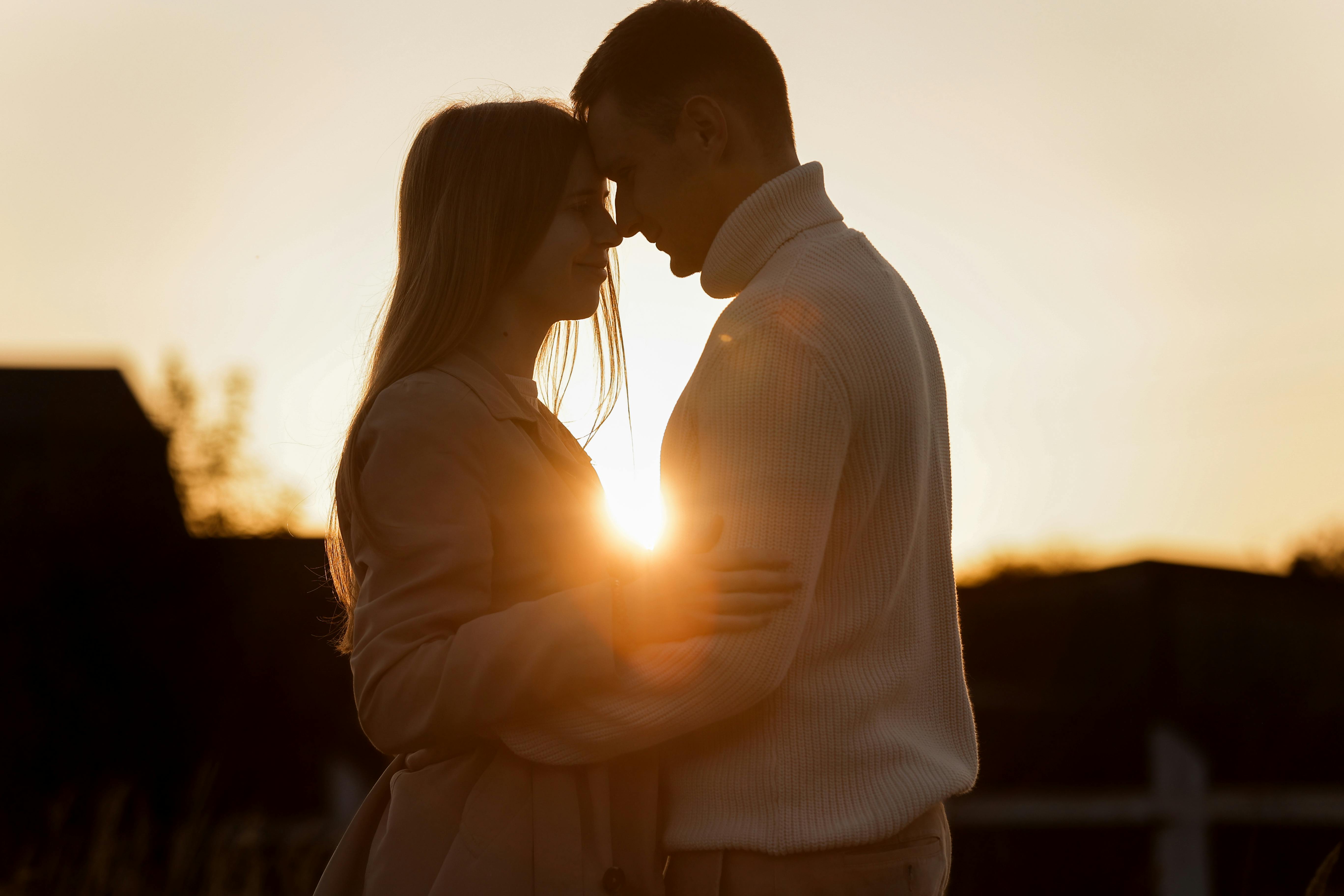 Silhouette of loving couple couple at sunset is hugging and touching nose to nose outdoors at park. Young man and woman falling in love have romantic date on Valentine's day.