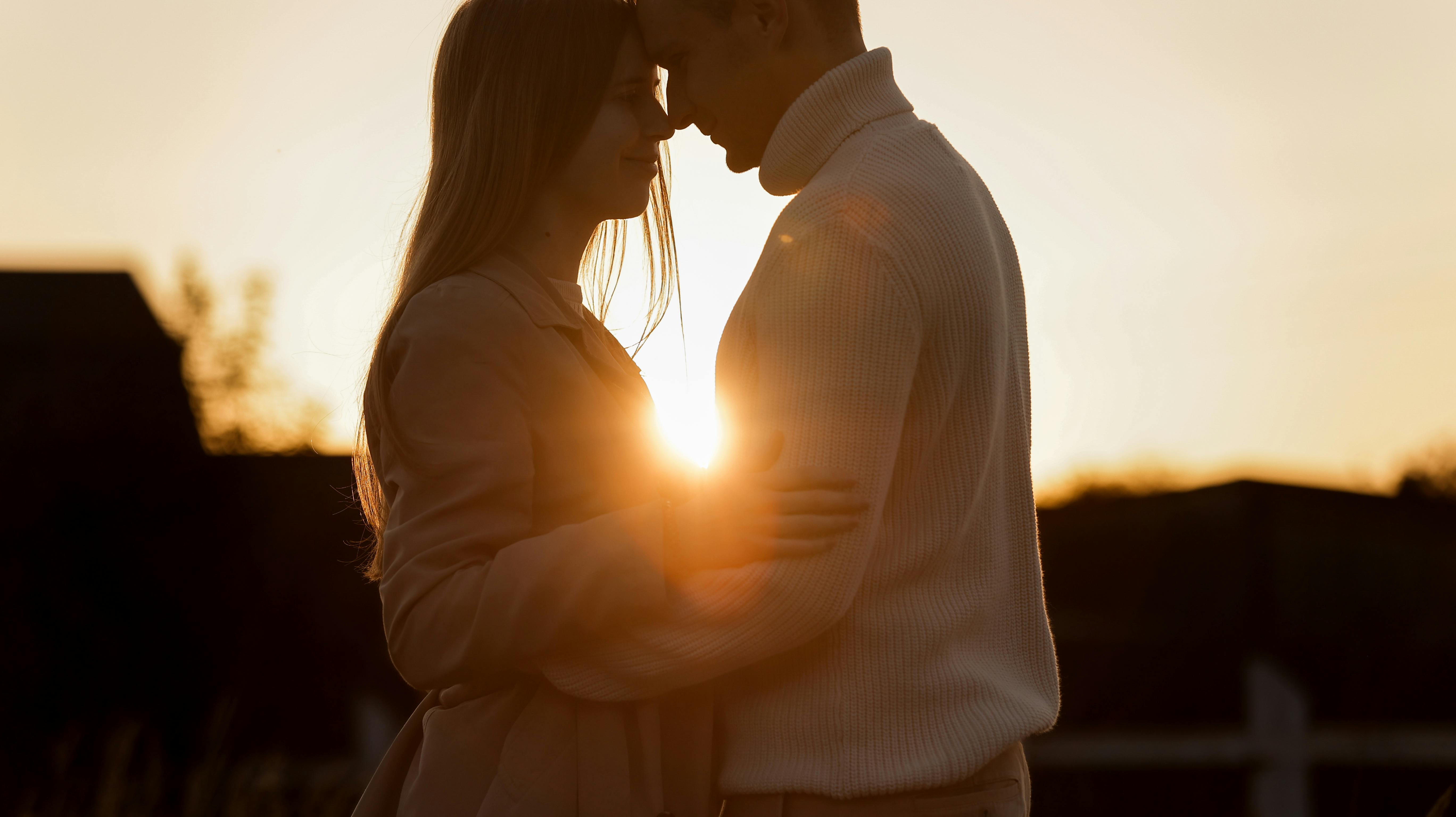 Silhouette of loving couple couple at sunset is hugging and touching nose to nose outdoors at park. Young man and woman falling in love have romantic date on Valentine's day.