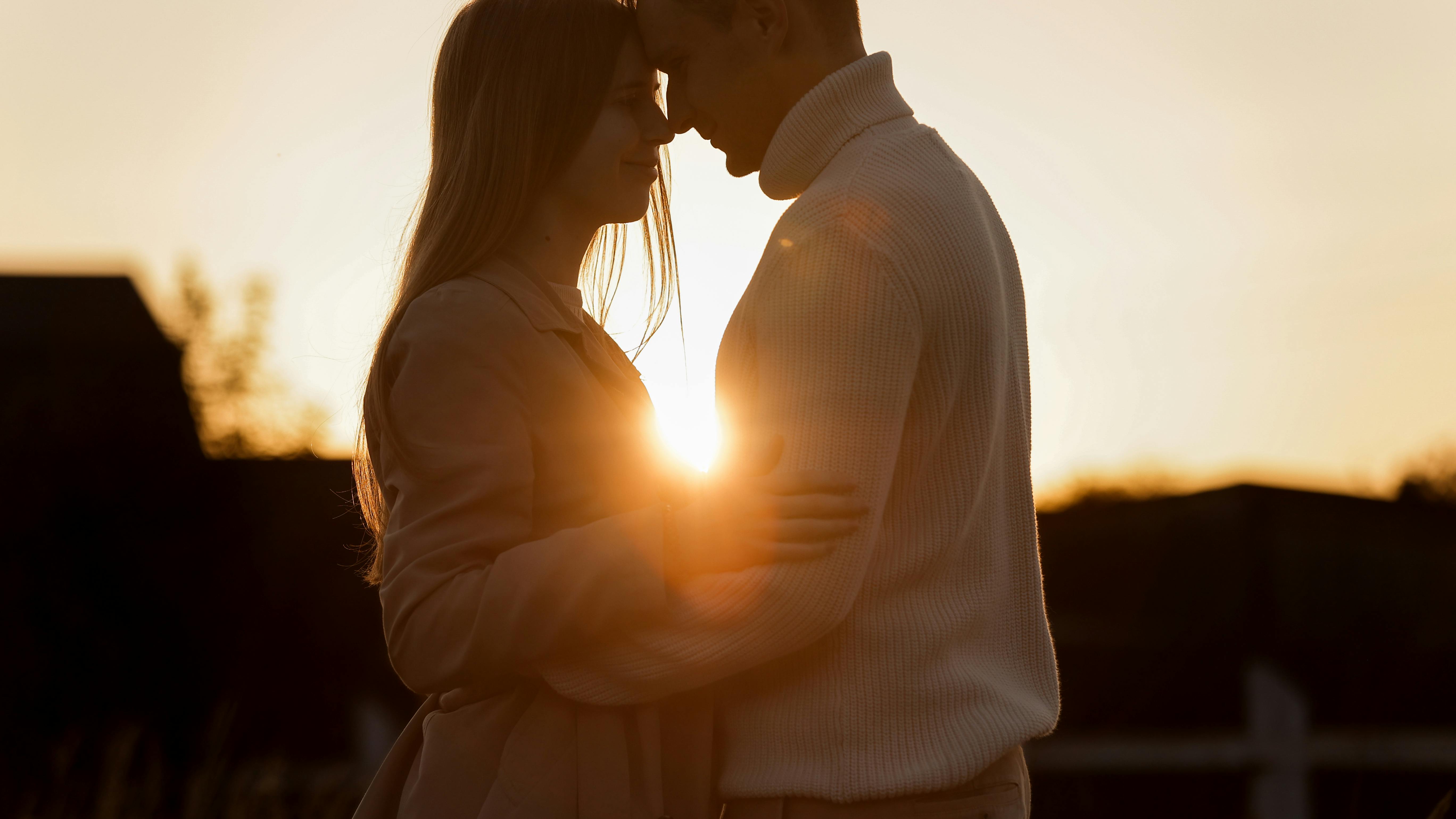Silhouette of loving couple couple at sunset is hugging and touching nose to nose outdoors at park. Young man and woman falling in love have romantic date on Valentine's day.