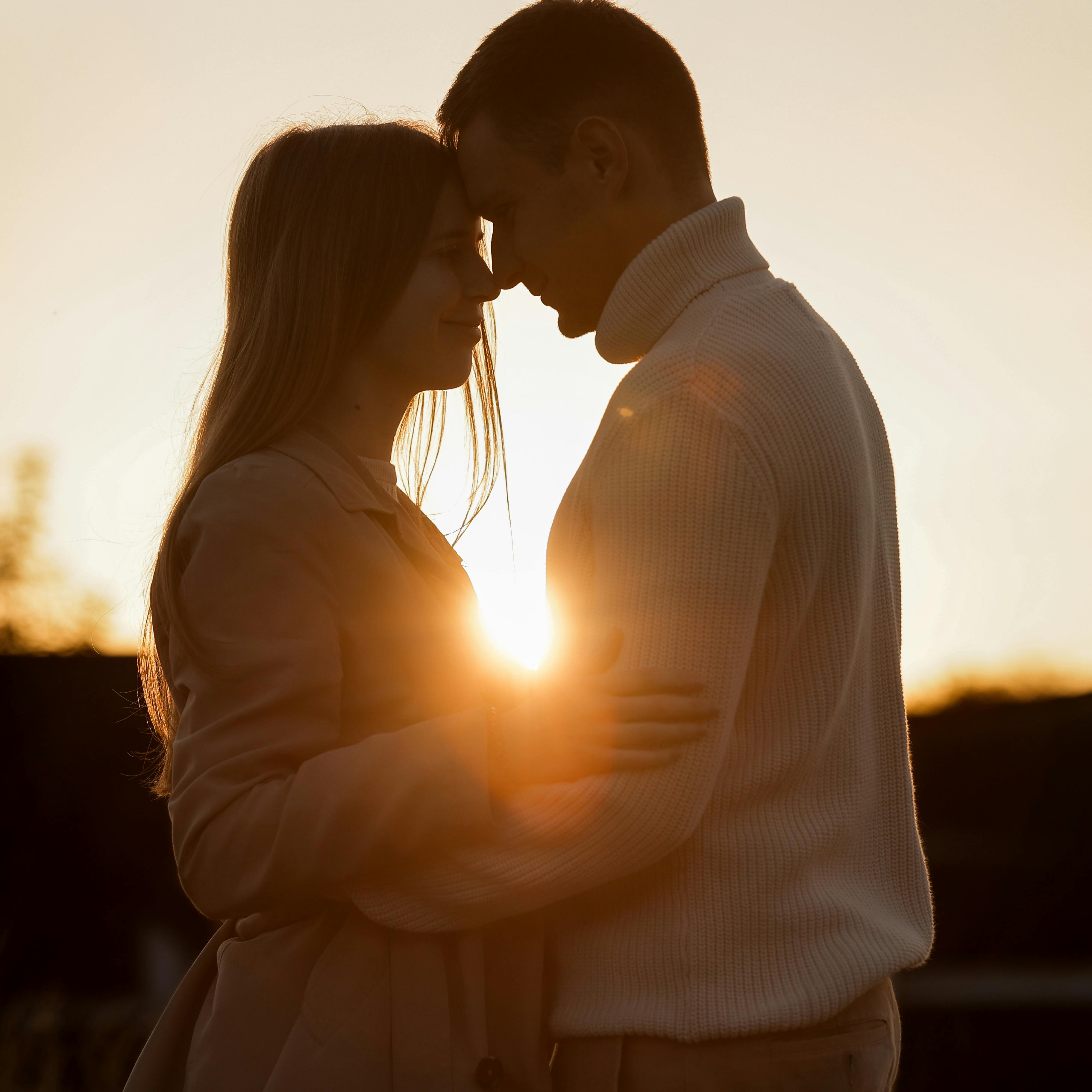 Silhouette of loving couple couple at sunset is hugging and touching nose to nose outdoors at park. Young man and woman falling in love have romantic date on Valentine's day.
