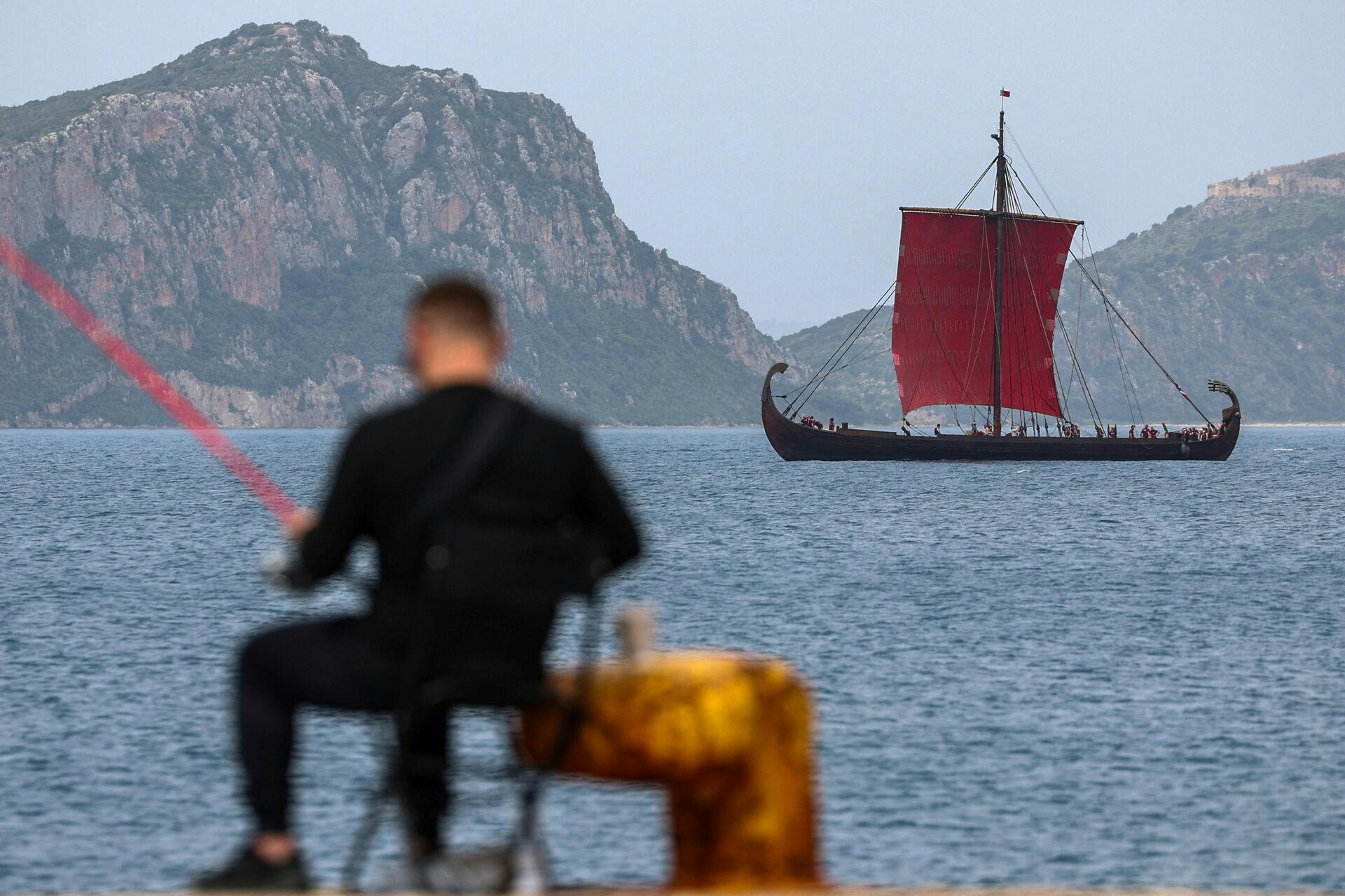 En mand fisker, mens en replika af et antikt krigsskib ses i baggrunden under optagelserne af "The Odyssey" i byen Pylos, Grækenland, den 16. marts 2025. 