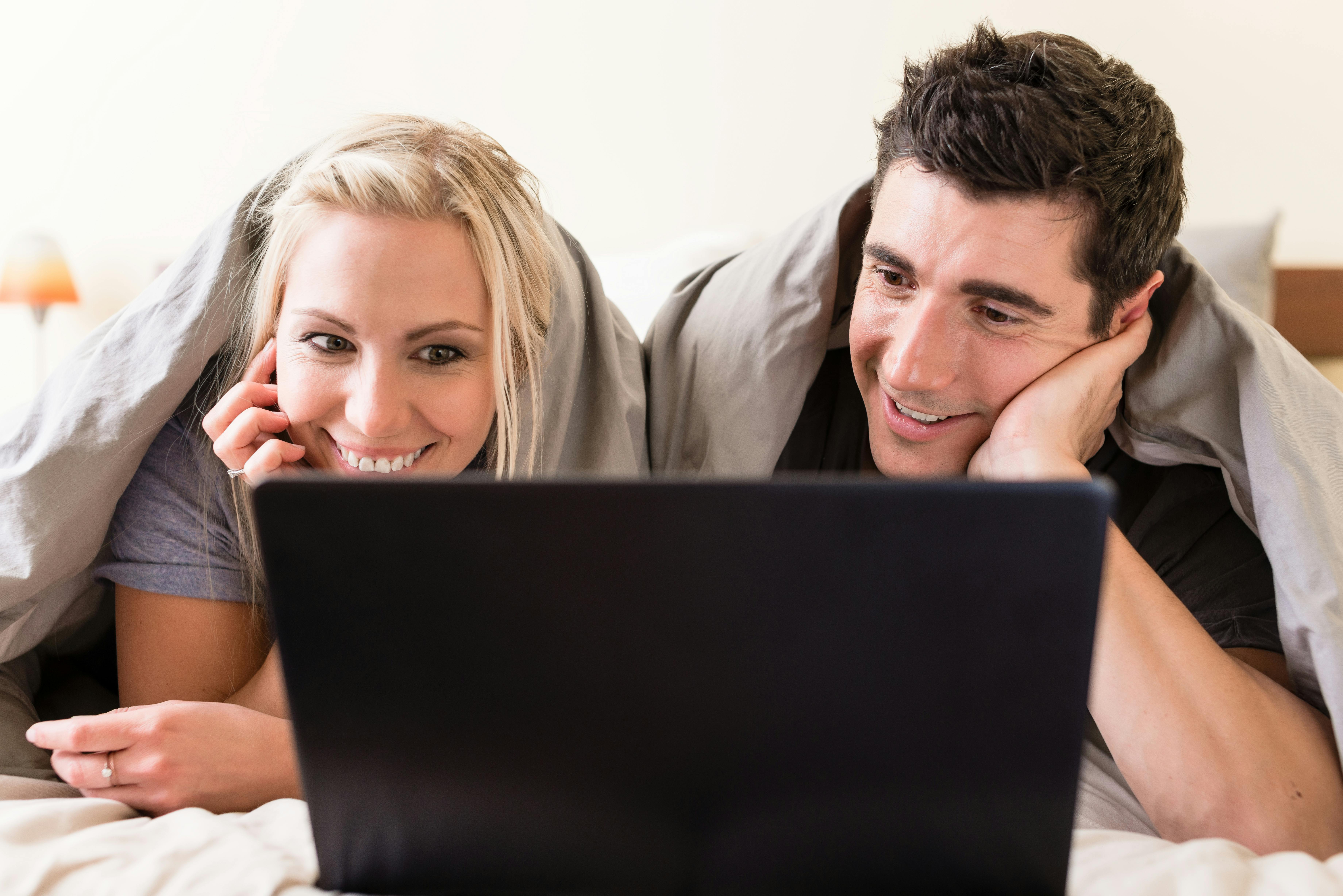 Young couple watching a funny movie or browsing the internet on laptop while lying down in bed