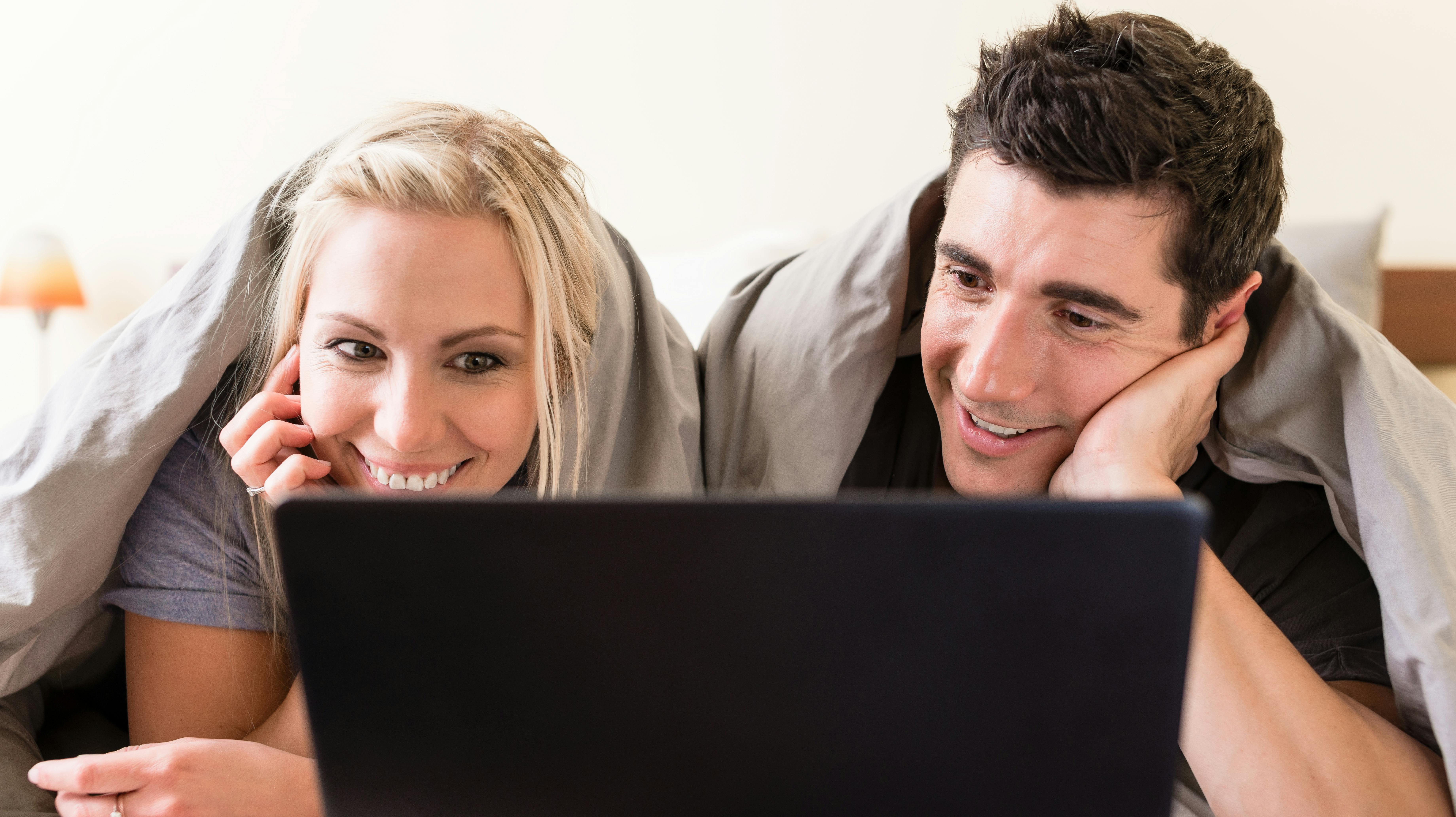 Young couple watching a funny movie or browsing the internet on laptop while lying down in bed