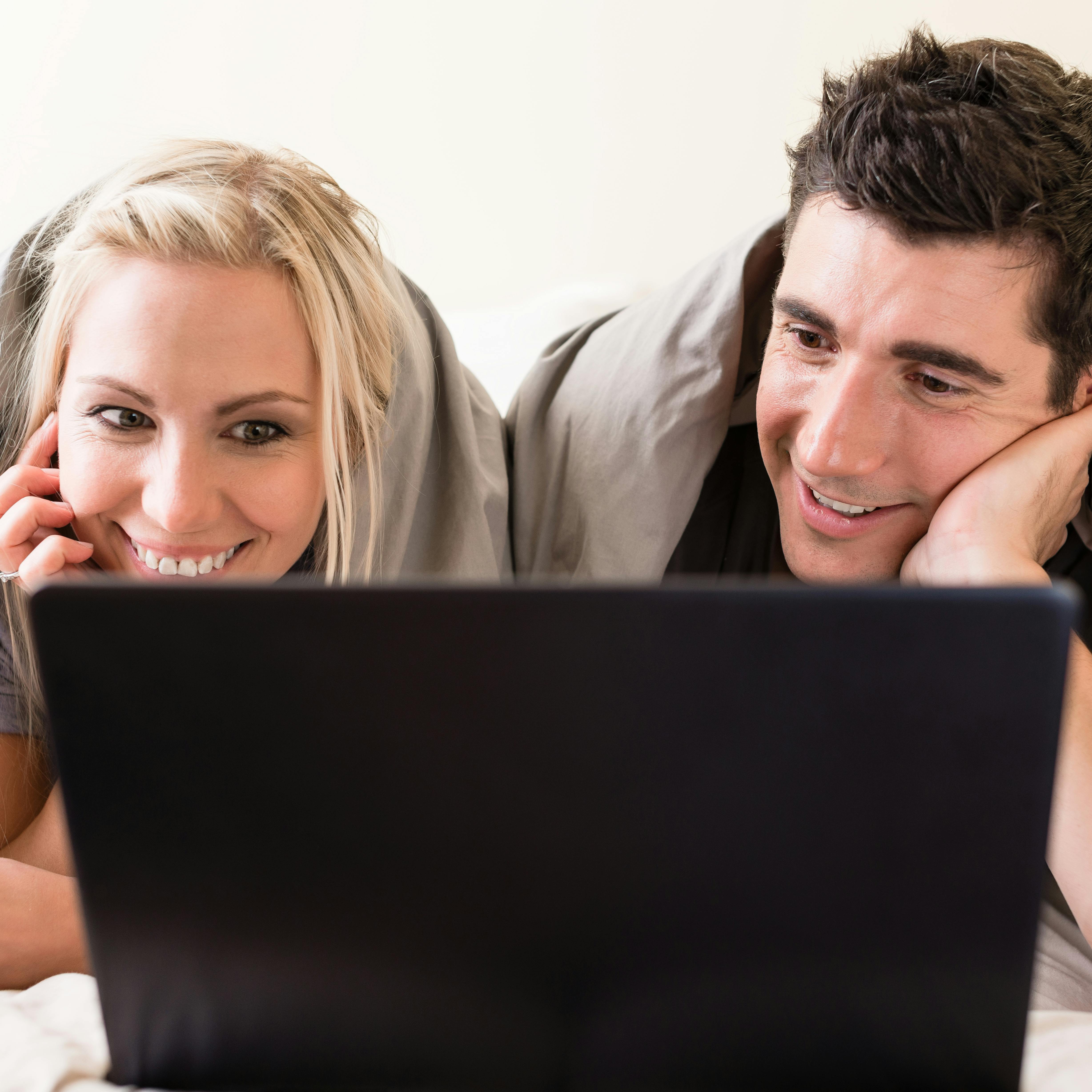 Young couple watching a funny movie or browsing the internet on laptop while lying down in bed
