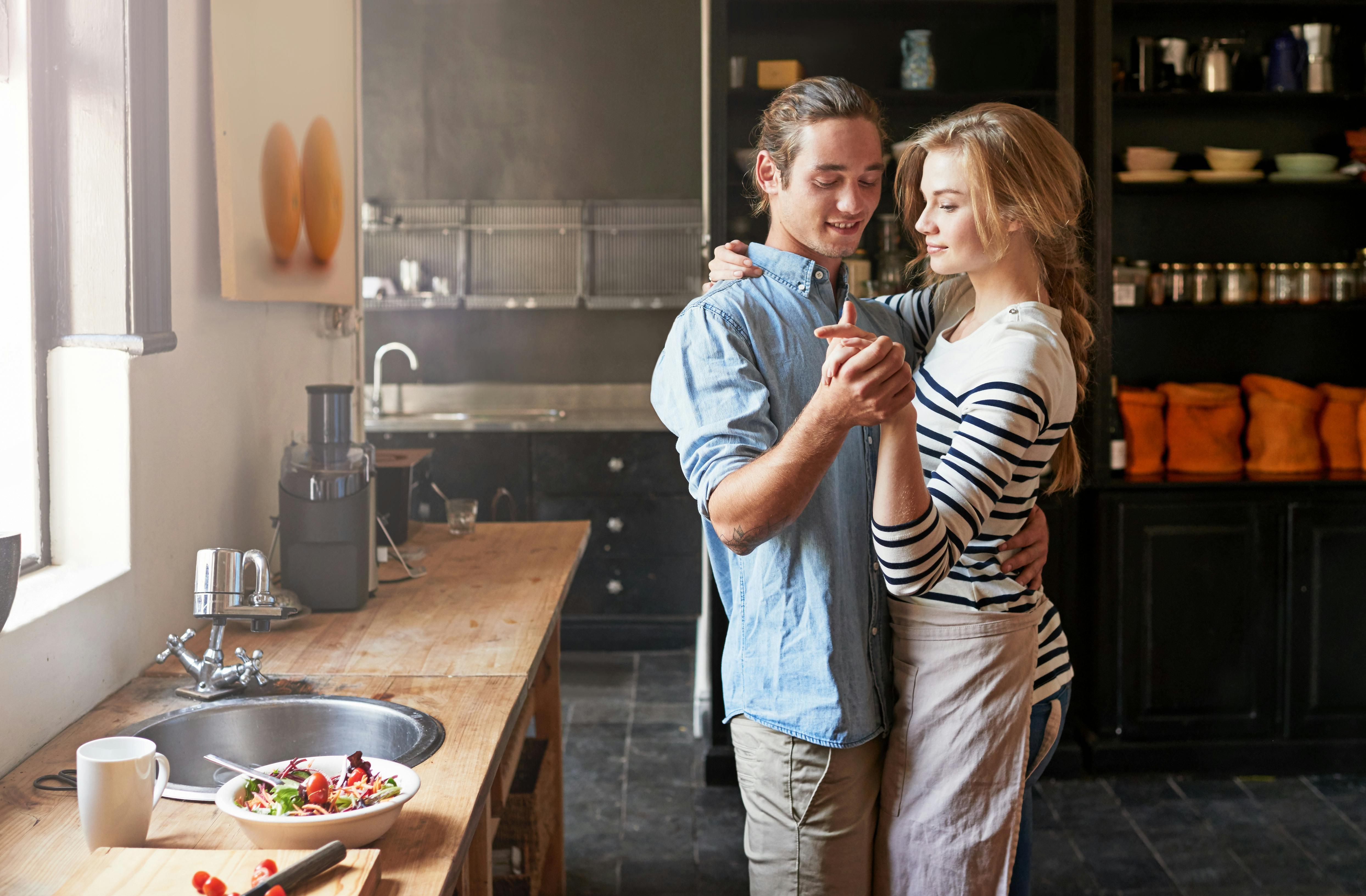Holding hands, dancing or couple with romance cooking in kitchen for food, meal prep or care. Smile, hug and people in apartment to celebrate anniversary for love at dinner, lunch or brunch in home.
