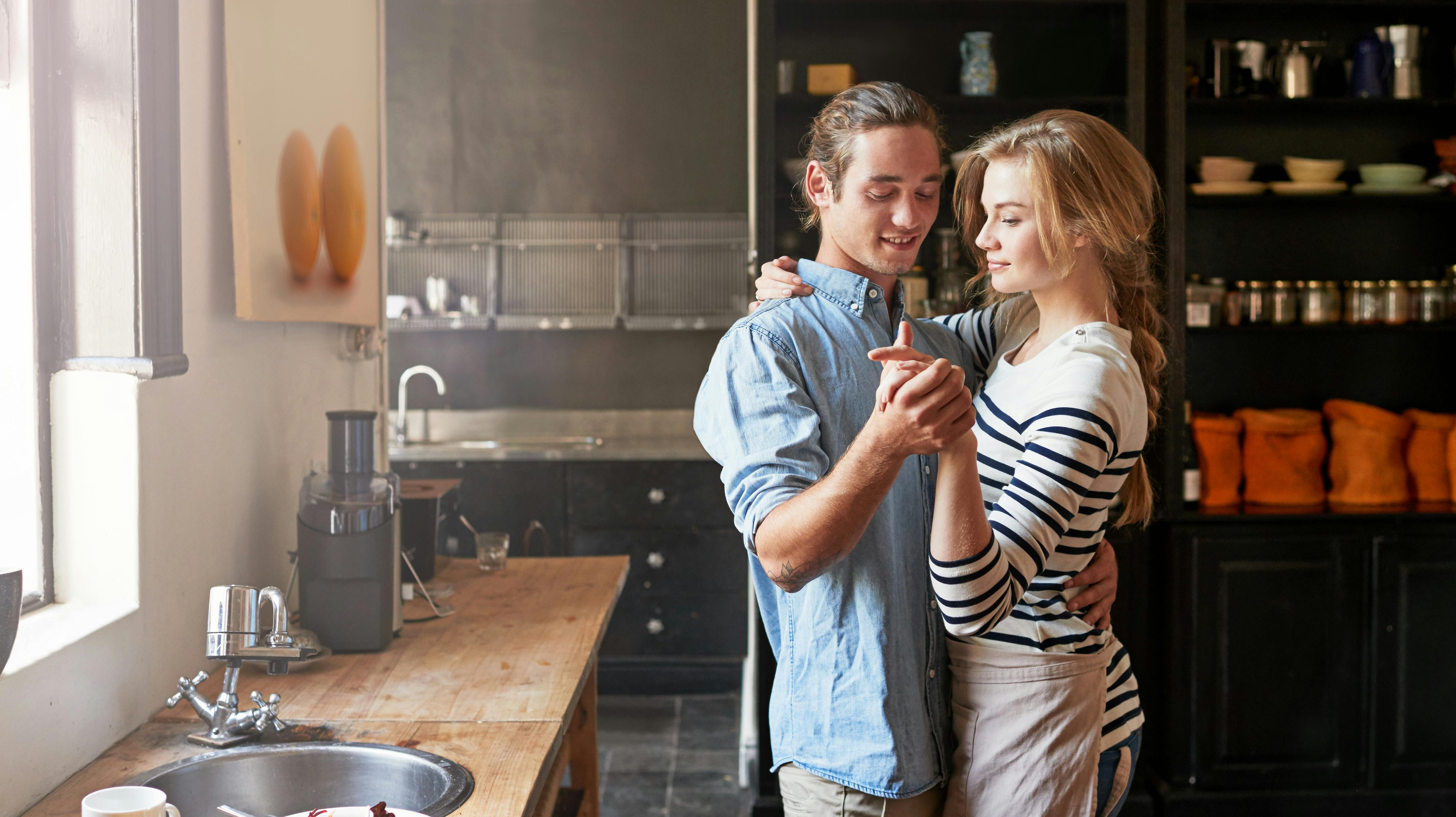 Holding hands, dancing or couple with romance cooking in kitchen for food, meal prep or care. Smile, hug and people in apartment to celebrate anniversary for love at dinner, lunch or brunch in home.