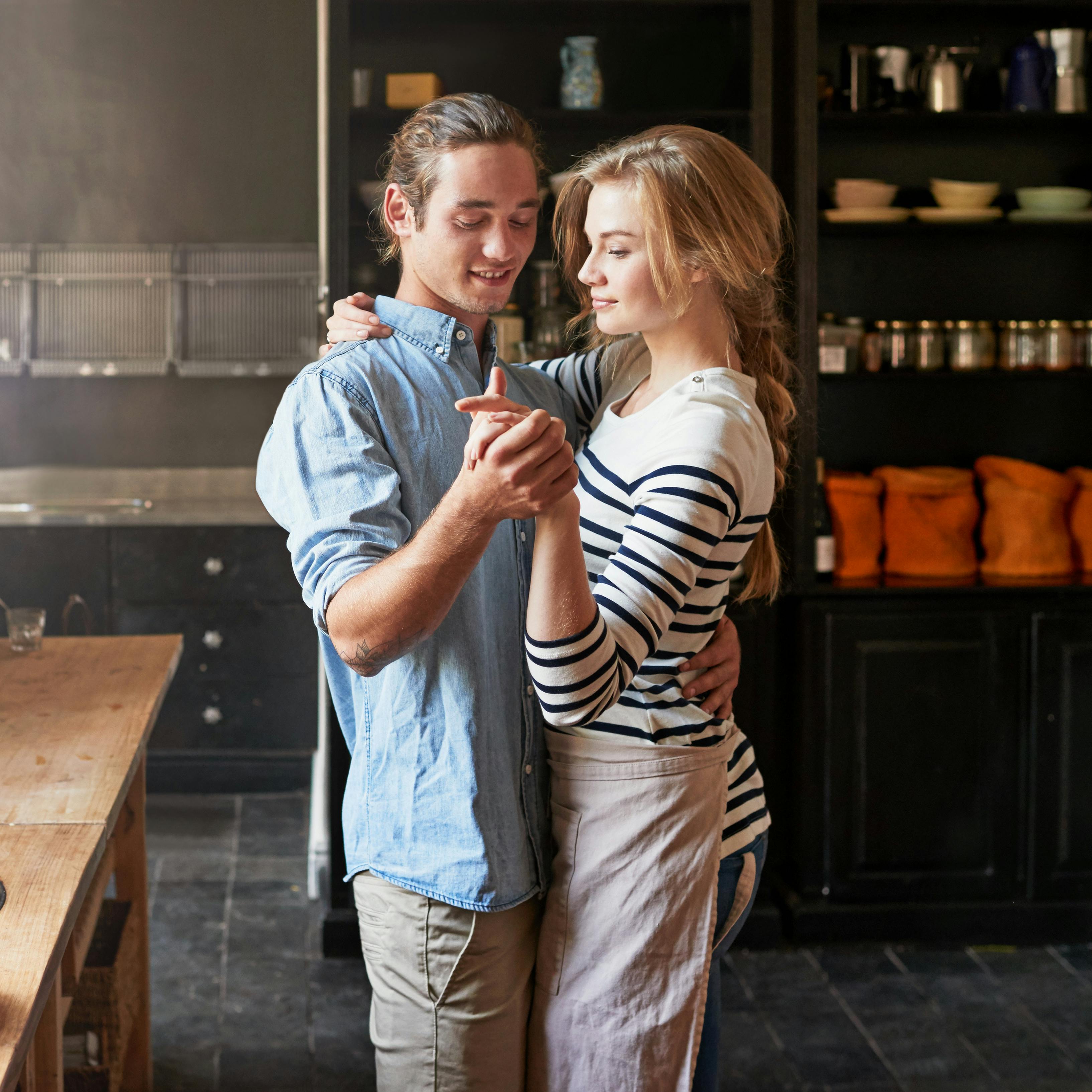 Holding hands, dancing or couple with romance cooking in kitchen for food, meal prep or care. Smile, hug and people in apartment to celebrate anniversary for love at dinner, lunch or brunch in home.