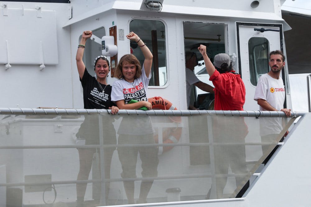 Den svenske aktivist Greta Thunberg (nr. 2 fra venstre) holder en knyttet næve i vejret, mens det skib, hun er om bord på, sejler ud fra havnen i Barcelona søndag. Omkring 20 skibe sejler i en flotille med kurs mod Gazastriben. - Foto: Eva Manez/Reuter