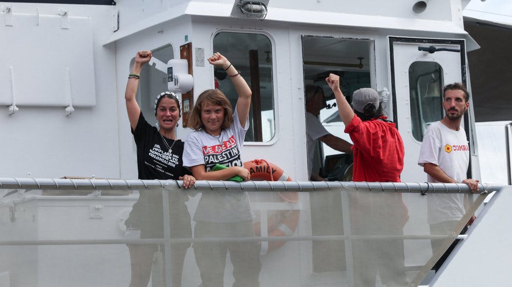 Den svenske aktivist Greta Thunberg (nr. 2 fra venstre) holder en knyttet næve i vejret, mens det skib, hun er om bord på, sejler ud fra havnen i Barcelona søndag. Omkring 20 skibe sejler i en flotille med kurs mod Gazastriben. - Foto: Eva Manez/Reuter