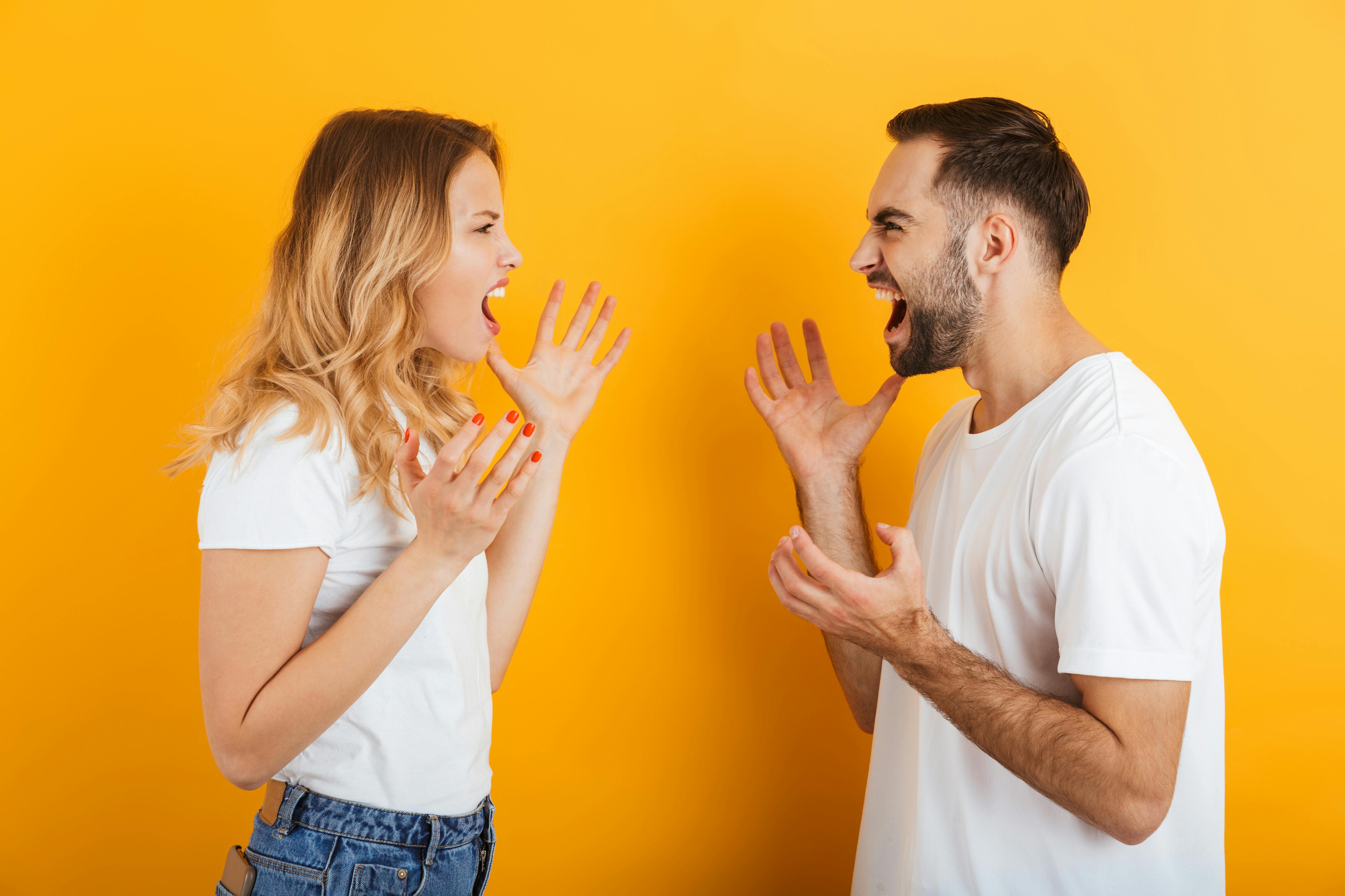 Image of furious couple man and woman in basic t-shirts screaming at each other during fight isolated over yellow background