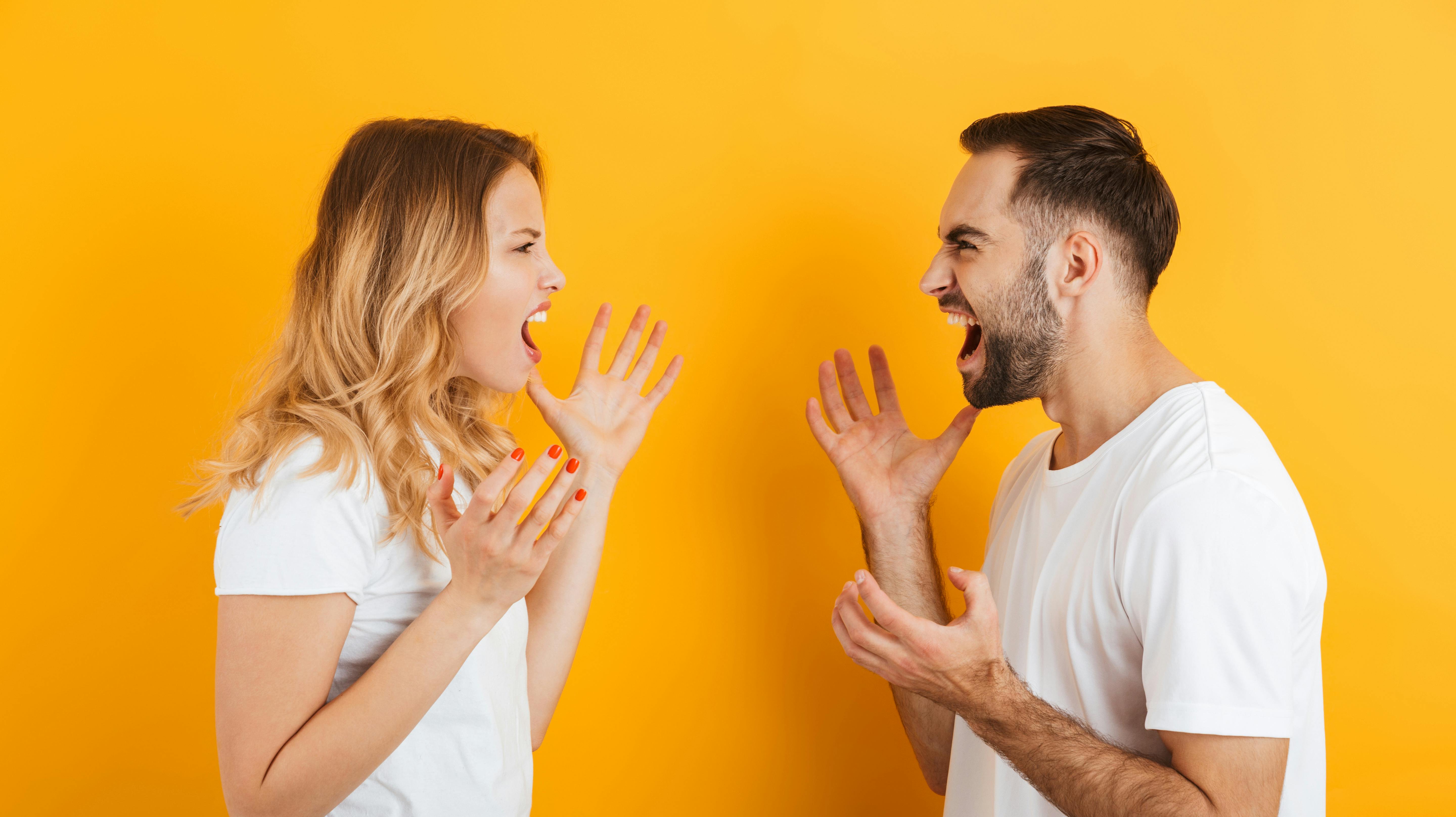 Image of furious couple man and woman in basic t-shirts screaming at each other during fight isolated over yellow background
