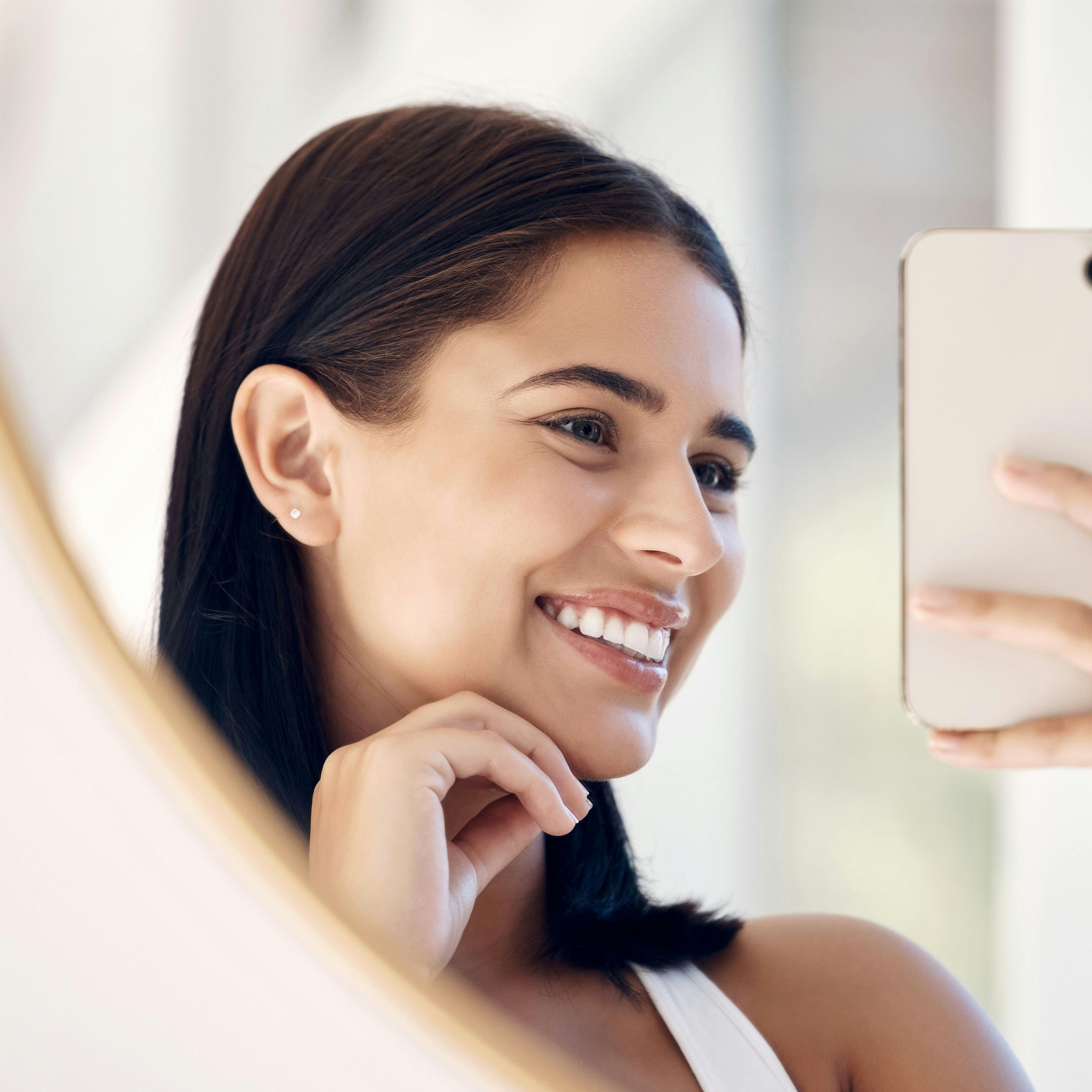 Phone, happy and selfie of woman in bathroom with smile for natural social media beauty in mirror. Reflection, happiness and skincare of wellness influencer girl with smartphone in the morning